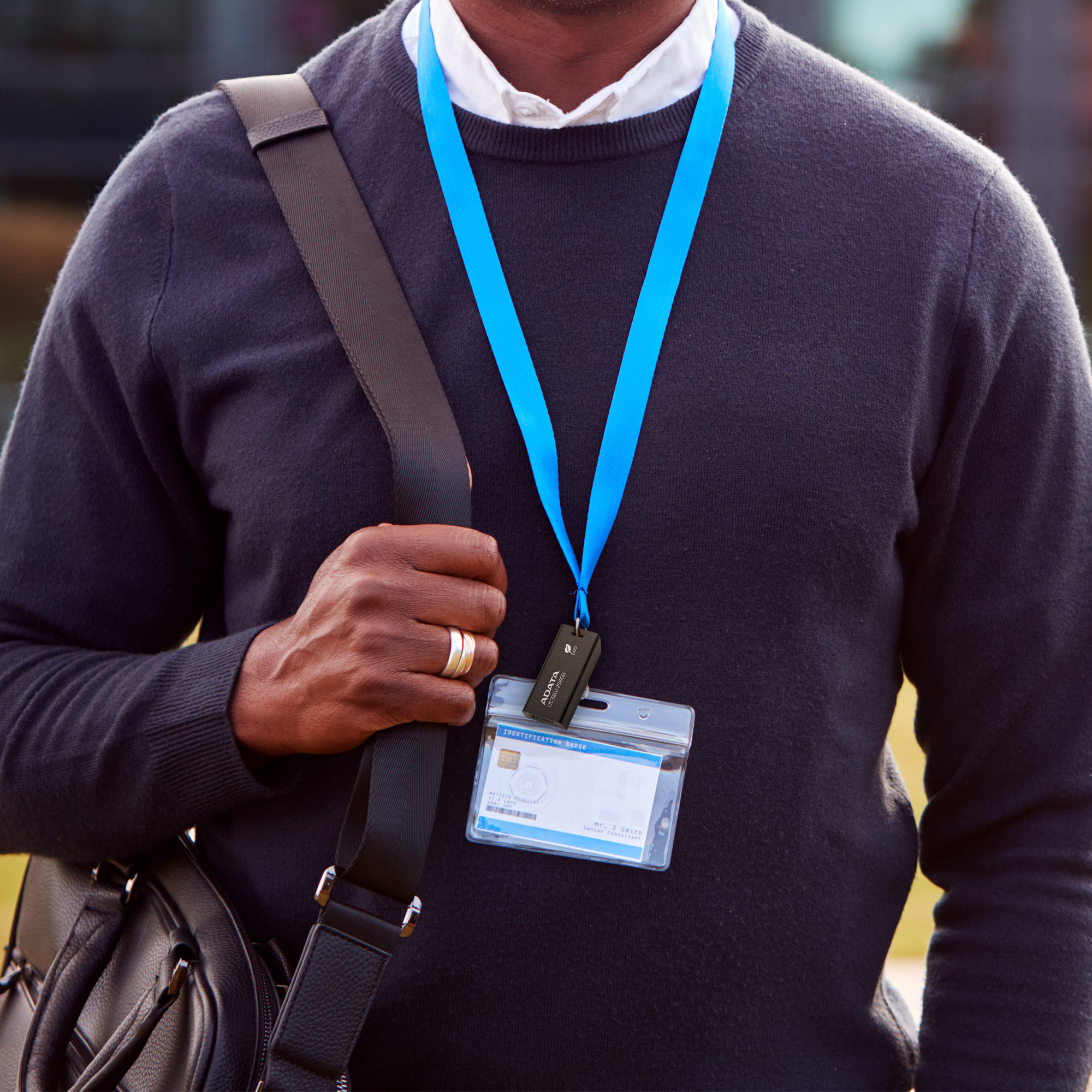 Mężczyzna noszący smycz i torbę. Smycz trzyma przezroczysty uchwyt na kartę z dołączonym pendrivem.