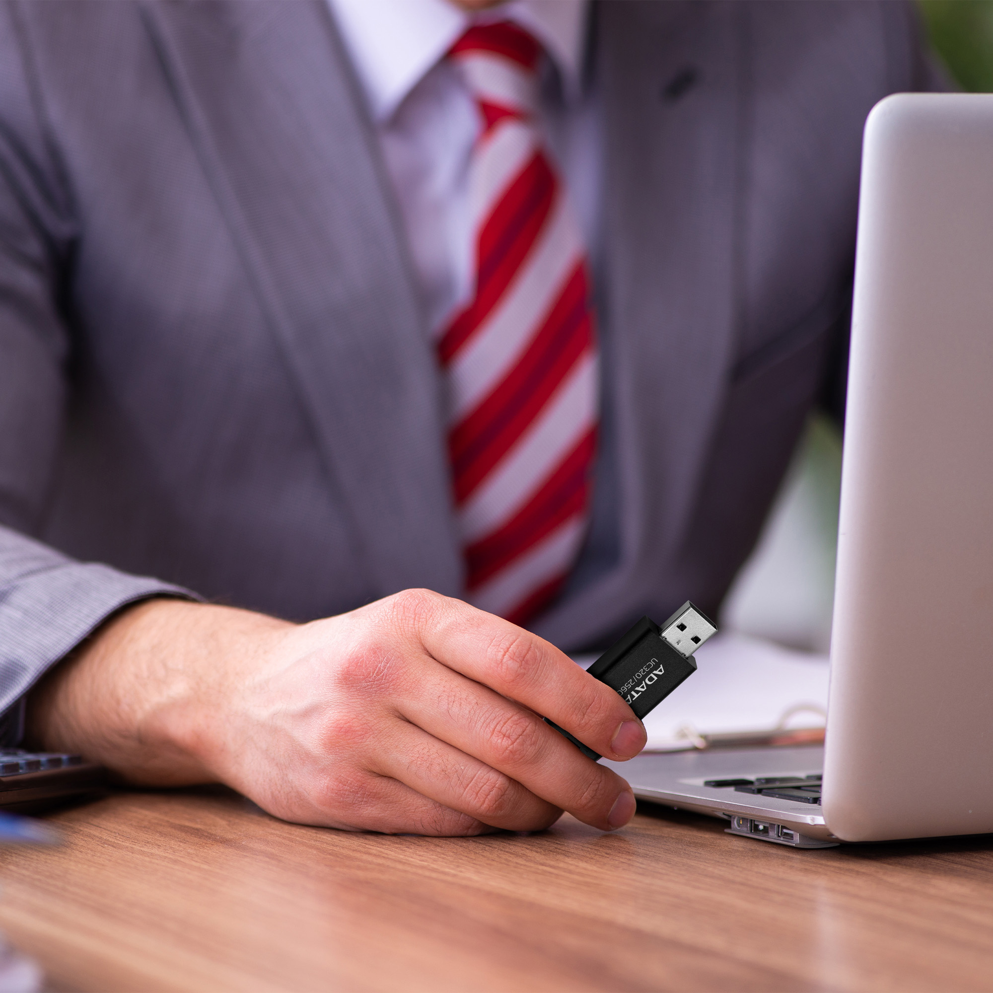 Mężczyzna w garniturze trzyma czarny pendrive obok laptopa.