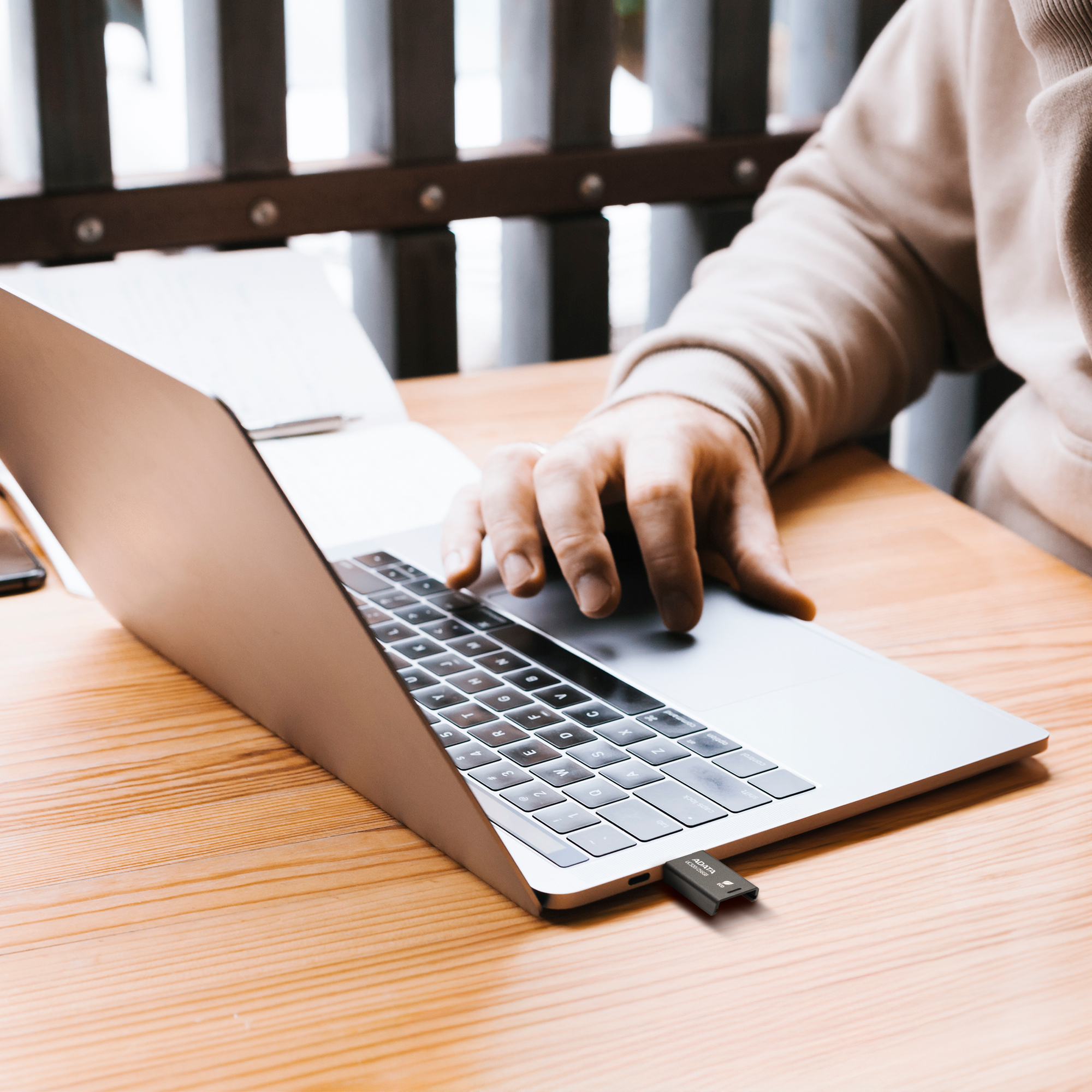 Osoba korzystająca z laptopa z podłączonym pendrivem USB. Laptop stoi na drewnianym stole.