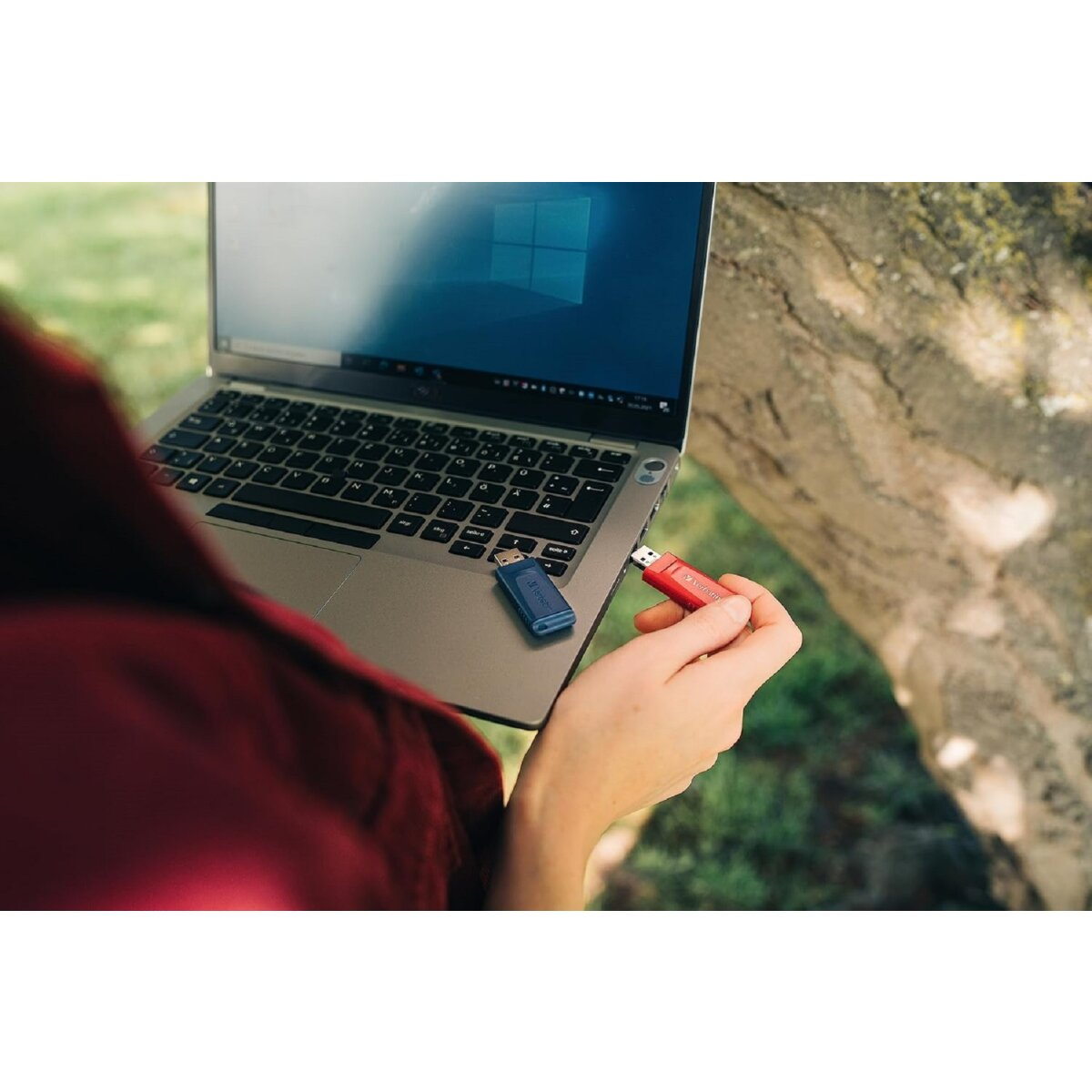 Osoba trzyma laptopa i dwa pendrive'y. Jeden czerwony, drugi niebieski.