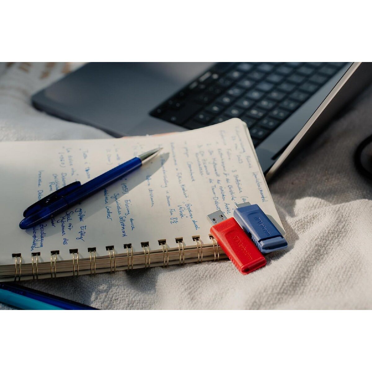 Notatnik, długopis i trzy pendrive'y na białej powierzchni.