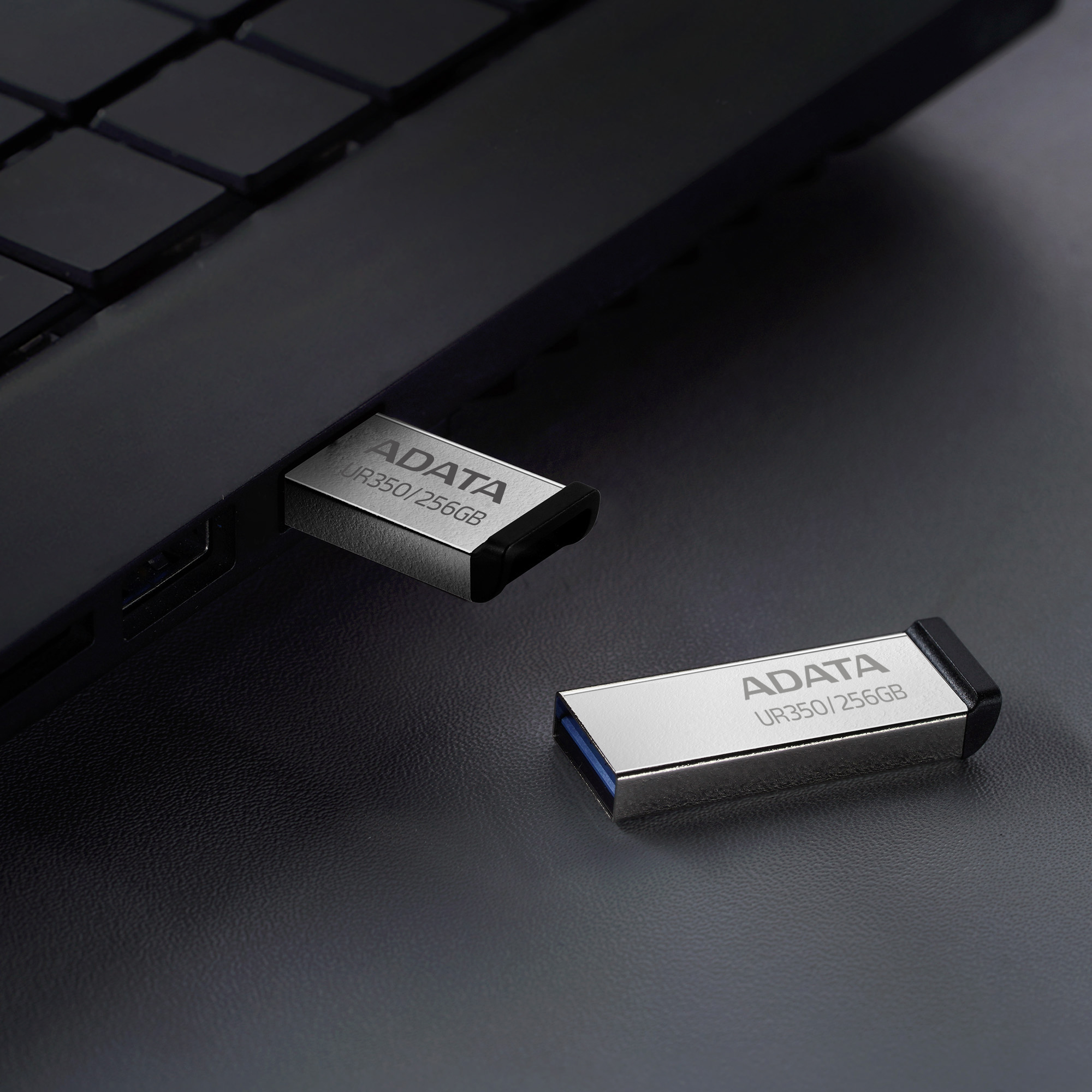 Dwa srebrne pendrive'y USB podłączone do laptopa.