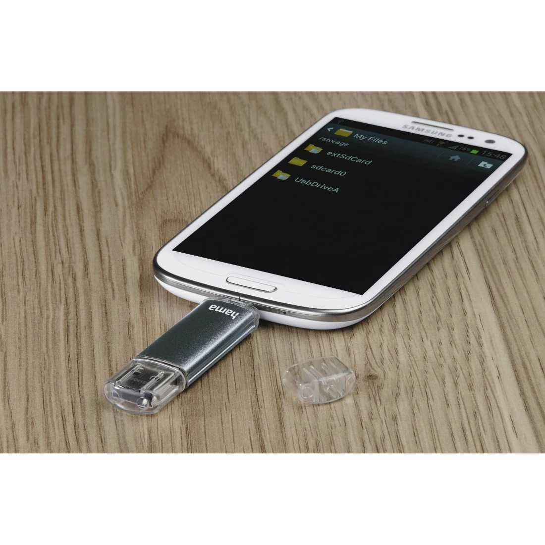 Srebrny pendrive USB podłączony do białego telefonu. Drewniane tło. Telefon wyświetla pliki.