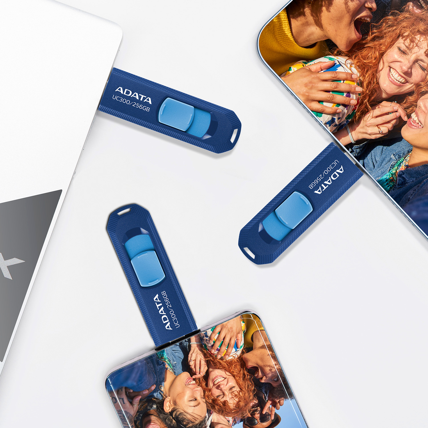 Trzy niebieskie pendrive'y ADATA na białej powierzchni. Zdjęcia ludzi w tle.