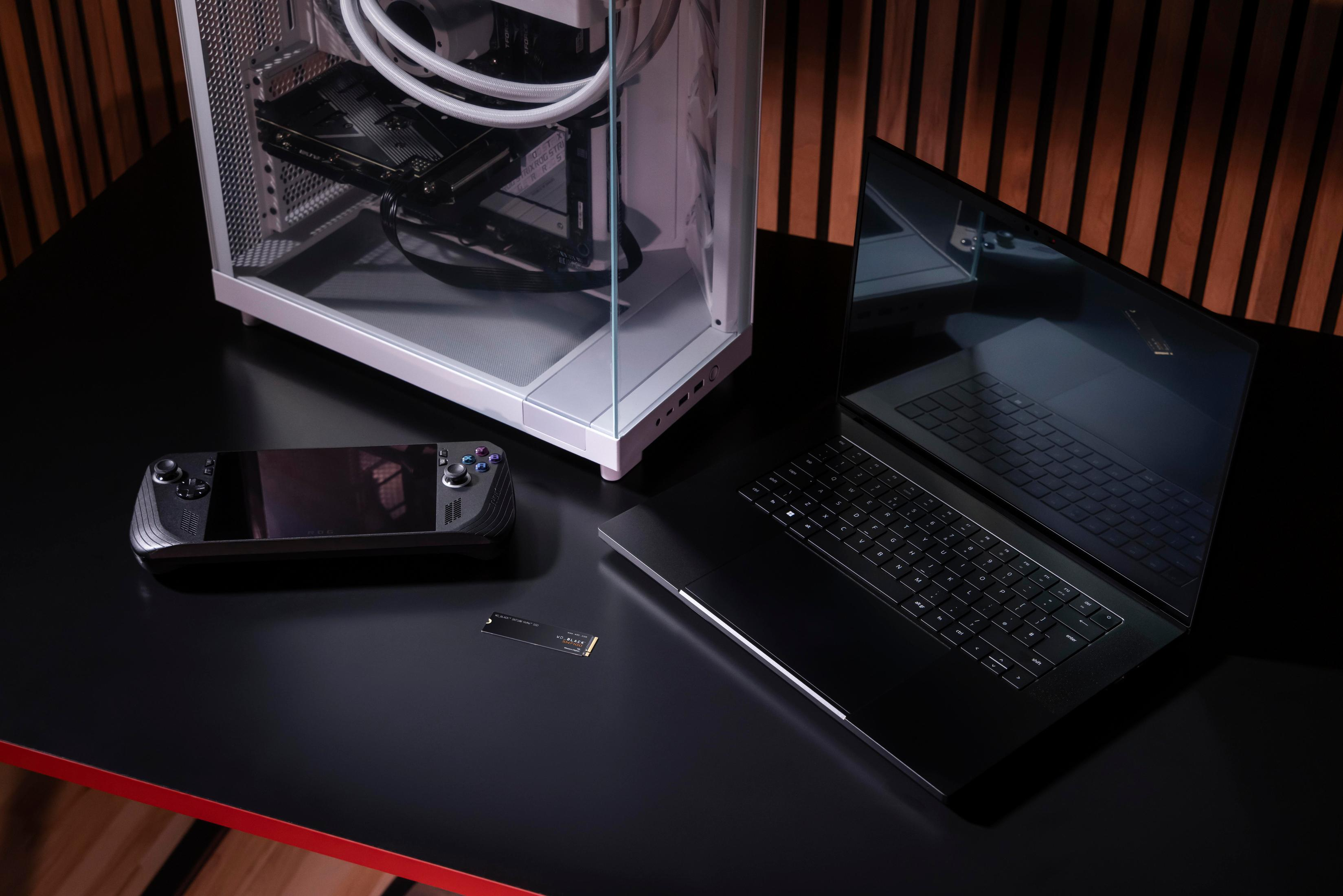 Konfiguracja biura z laptopem, obudową komputera i konsolą do gier na czarnym biurku.