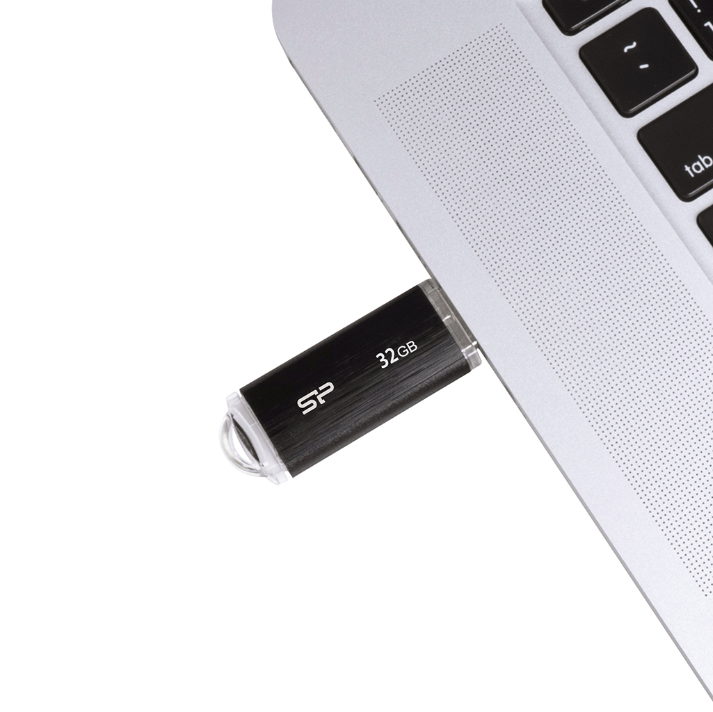 Czarny pendrive SP włożony do laptopa. Białe tło.