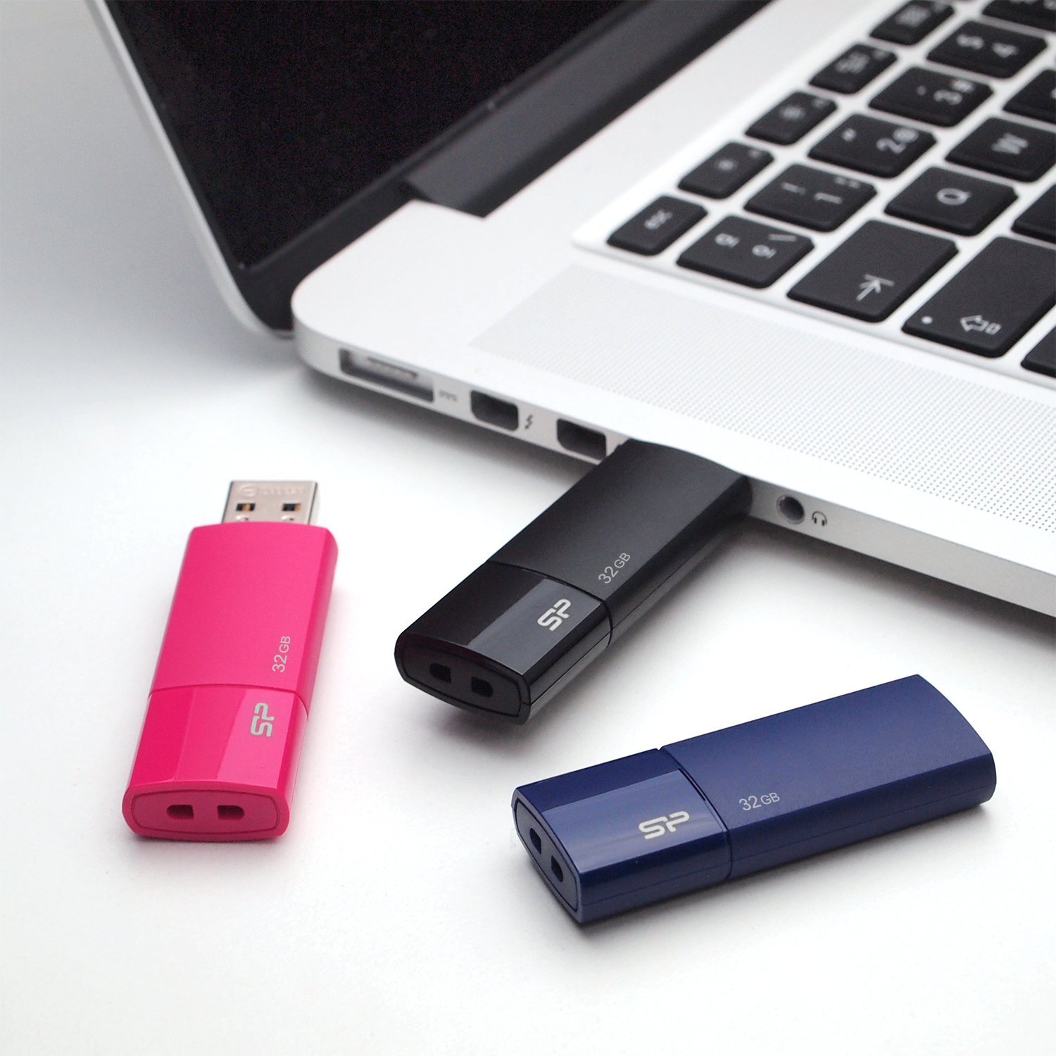Laptop con tre chiavette USB: rosa, nera e blu. Sfondo bianco.