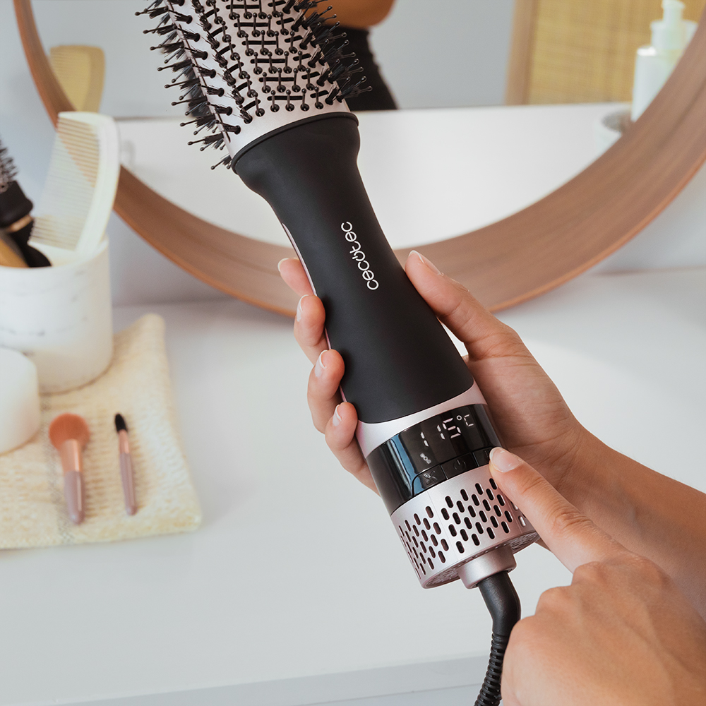 Kobieta trzymająca czarno-różowo-złotą szczotkę do włosów z wyświetlaczem temperatury.