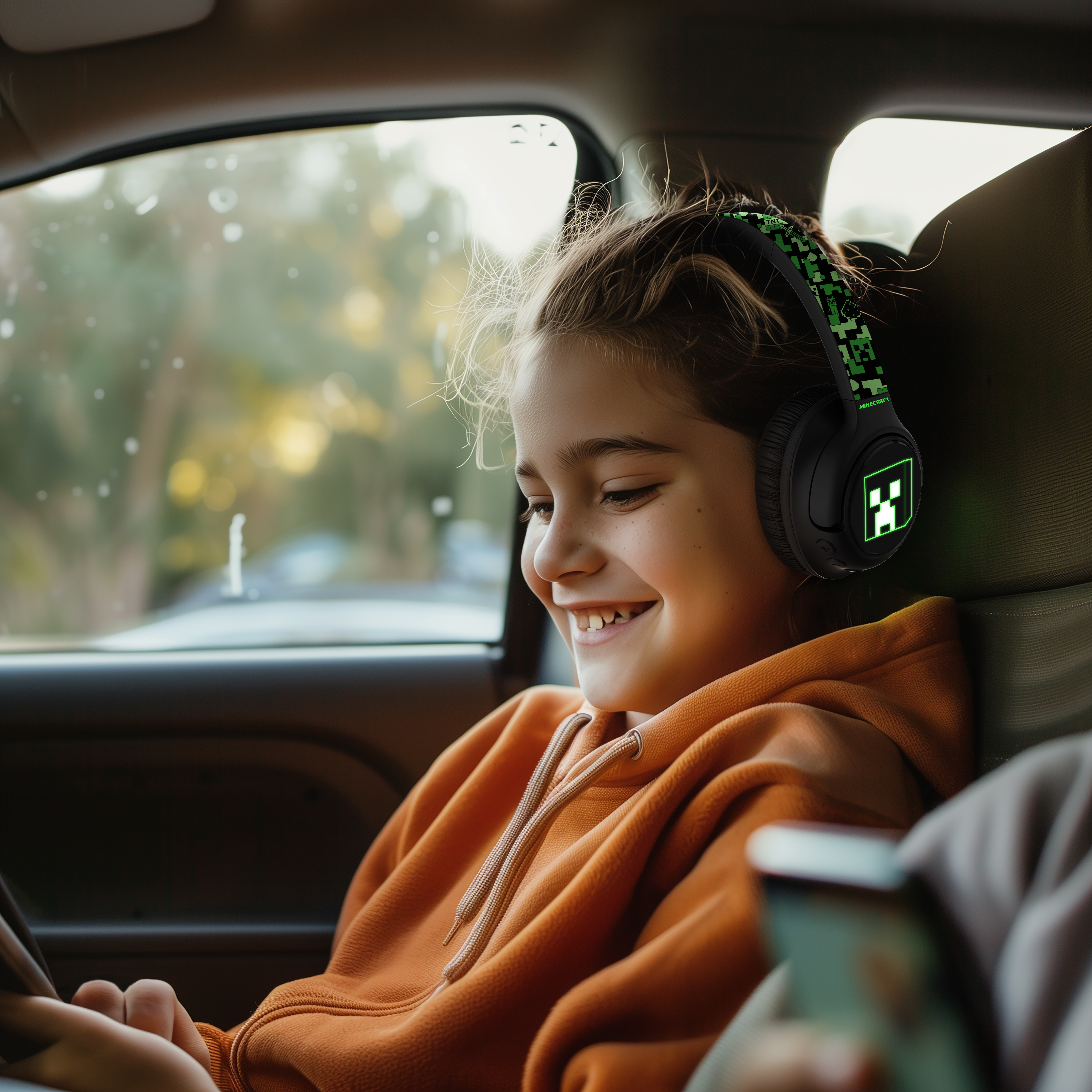 Ein Mädchen in einem orangefarbenen Kapuzenpullover mit Minecraft-Kopfhörern, lächelnd in einem Auto.