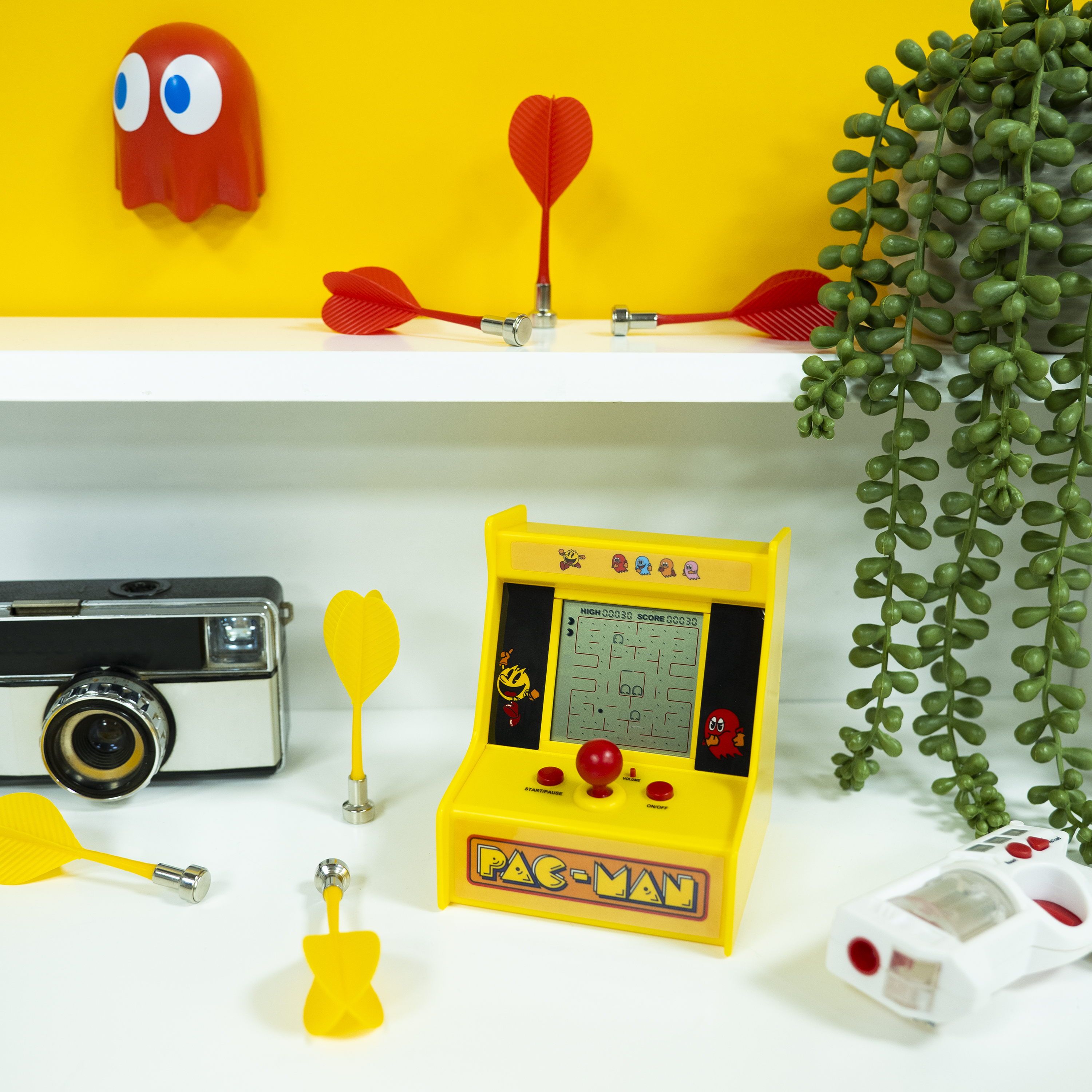 Een gele Pac-Man arcadegame met darts en andere decoraties op een wit oppervlak.
