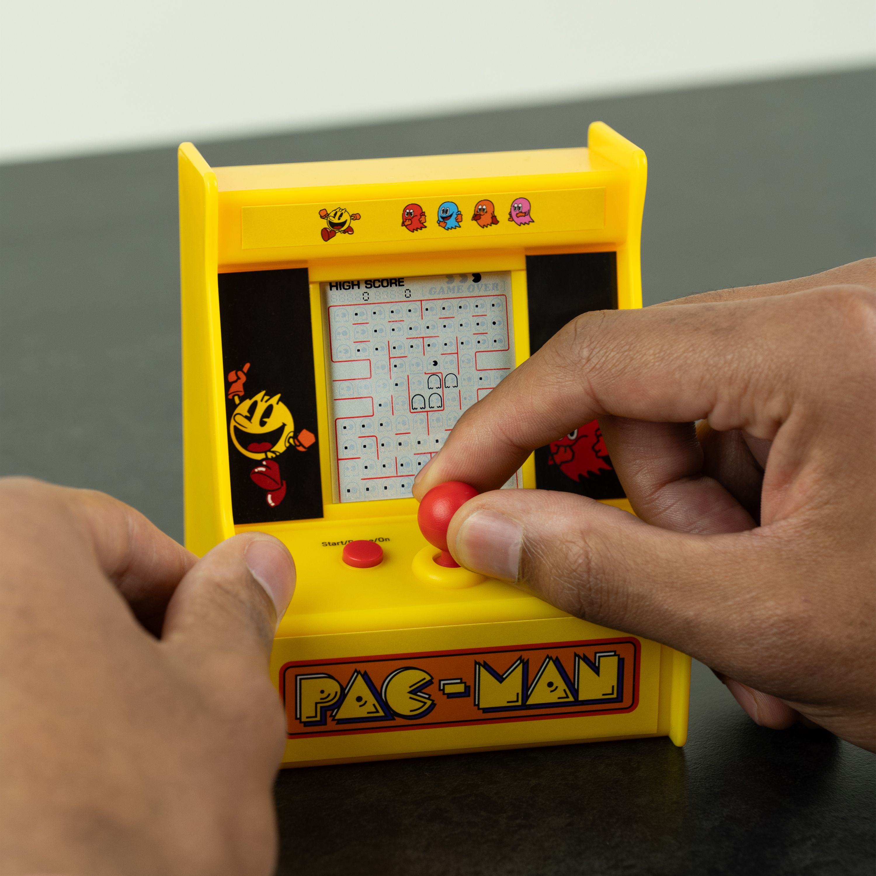 Handen die spelen met een gele Pac-Man game, rode joystick, zwarte achtergrond.