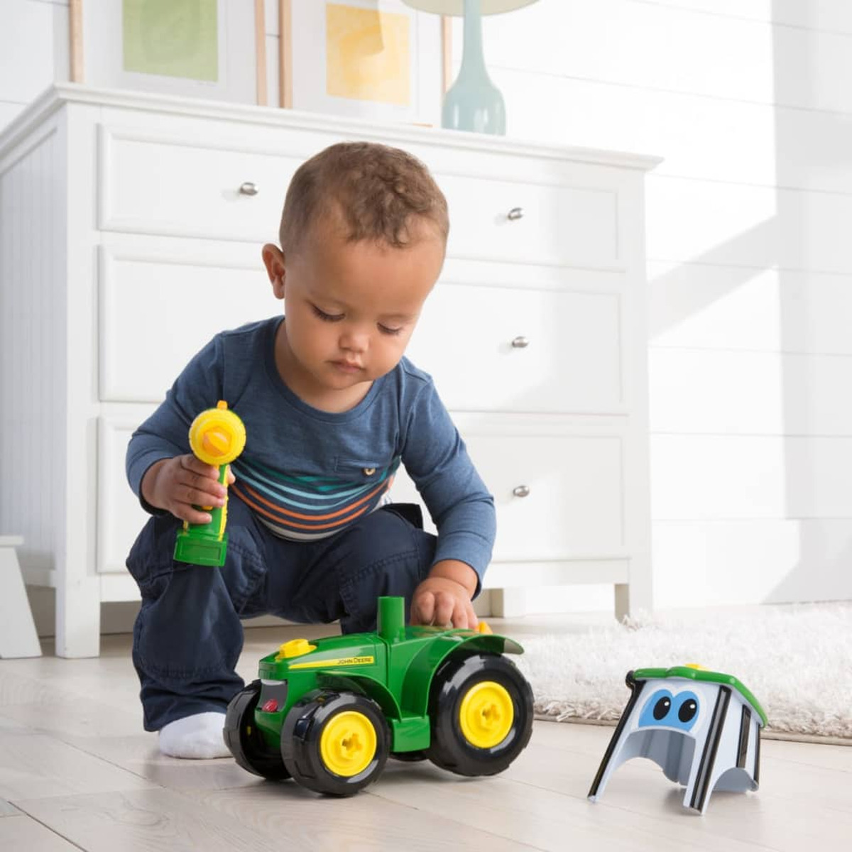 Ein Kleinkind spielt mit einem grünen Spielzeugtraktor und einem kleinen Schuppen.