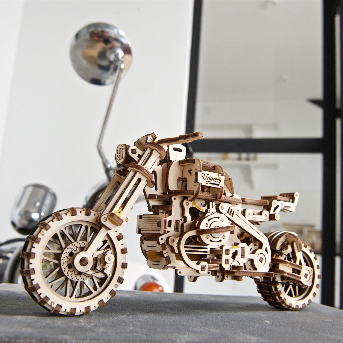 Drewniany model motocykla na ciemnej powierzchni ze srebrnym lustrem w tle. Jest to szczegółowa replika.