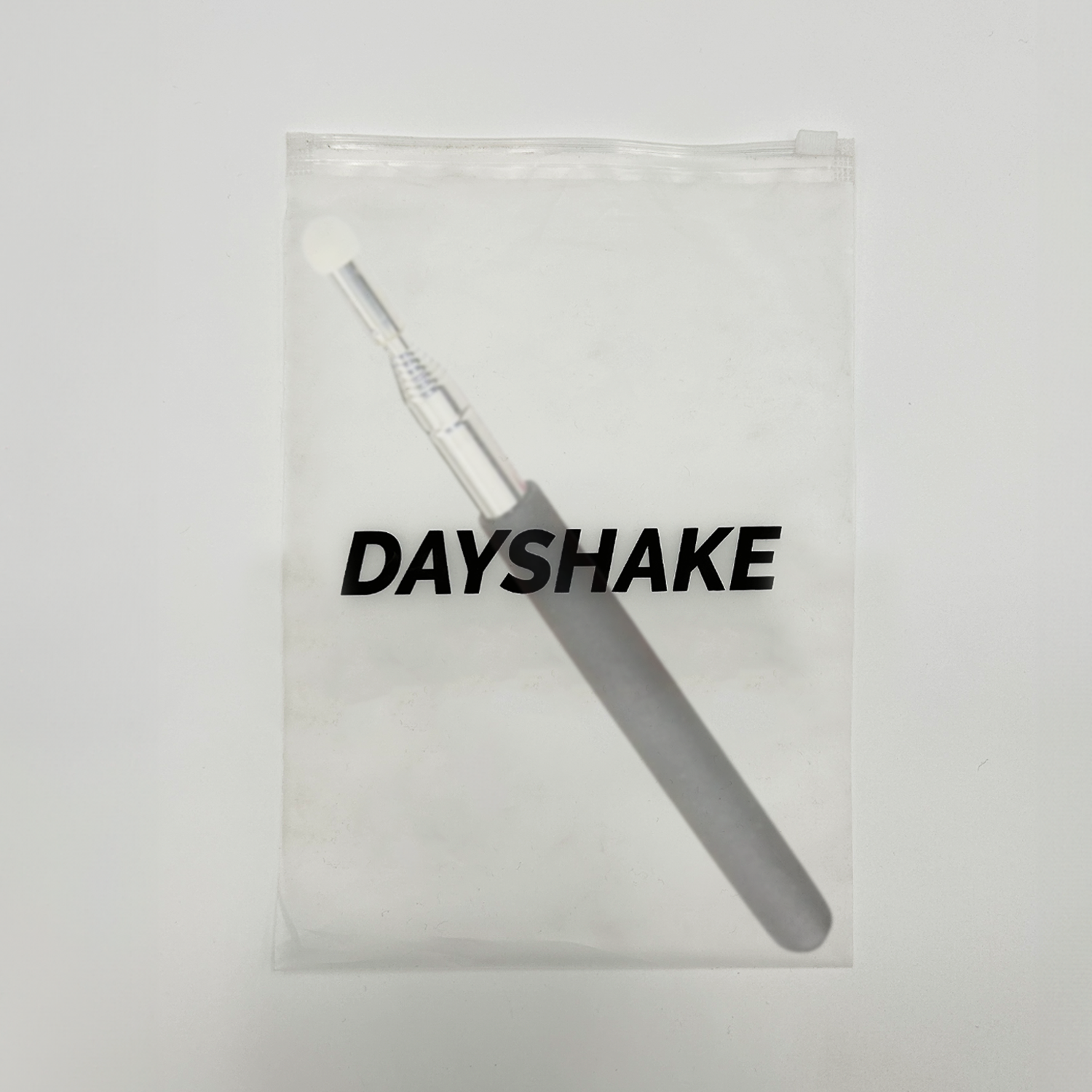 Transparente Plastiktüte mit 'DAYSHAKE'-Text und einem grauen Make-up-Pinsel.