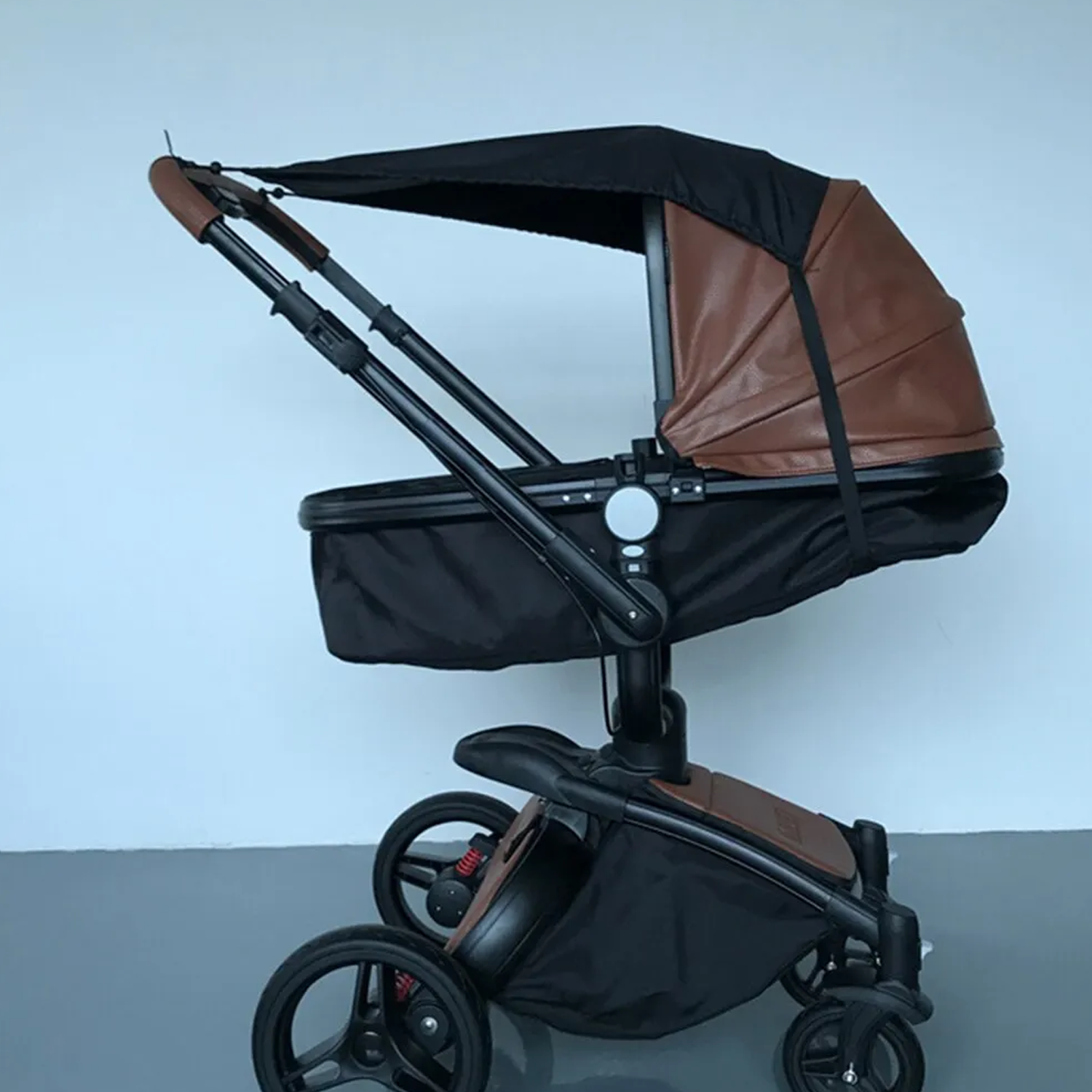 Ein schwarzer und brauner Kinderwagen mit braunem Verdeck, im Freien gezeigt.
