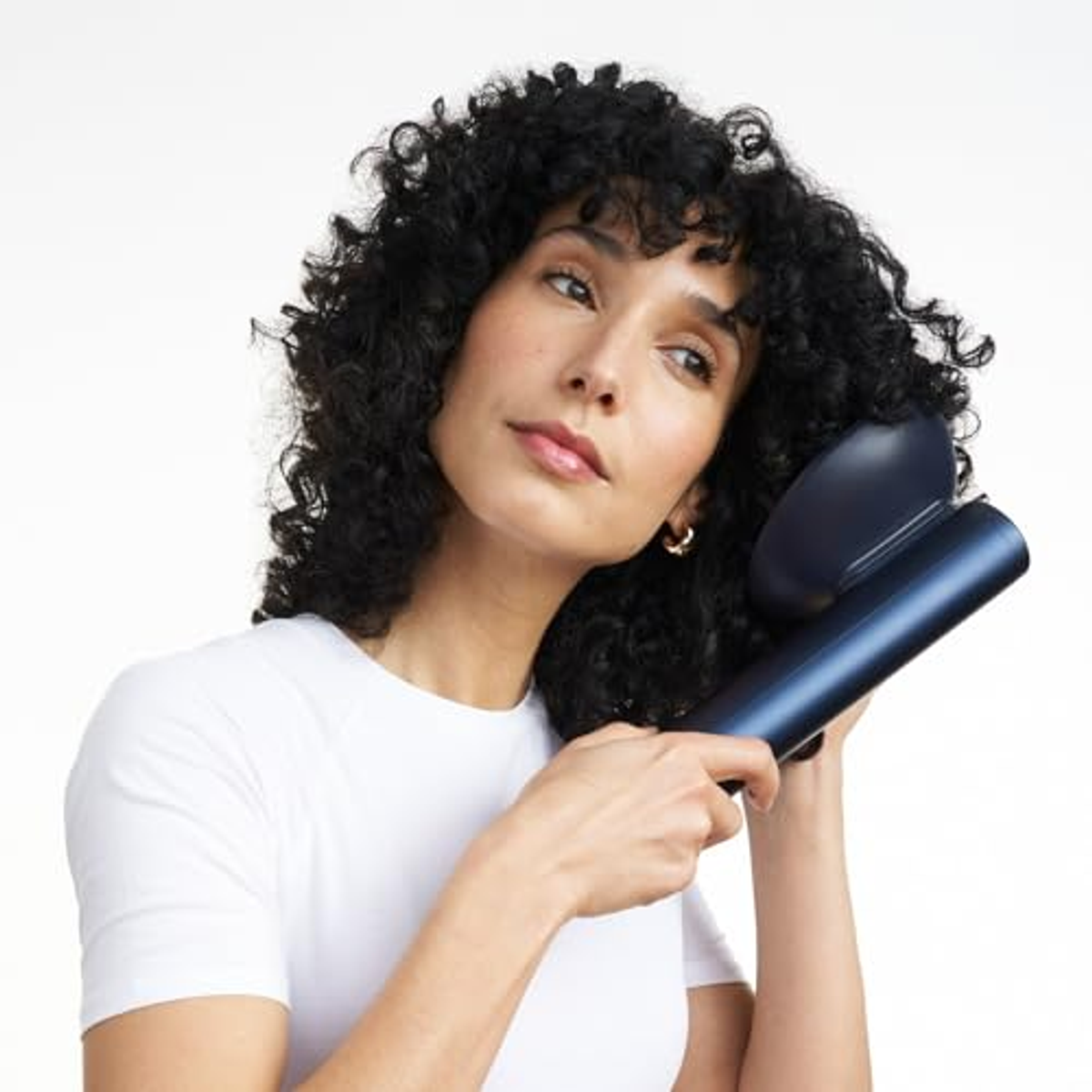 Donna con capelli ricci usa uno strumento blu per lo styling. Sfondo bianco.