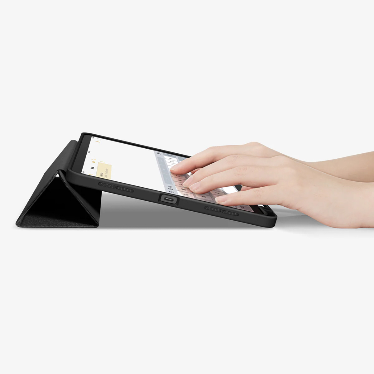 Hands typing on a black tablet with a case, on a white surface.
