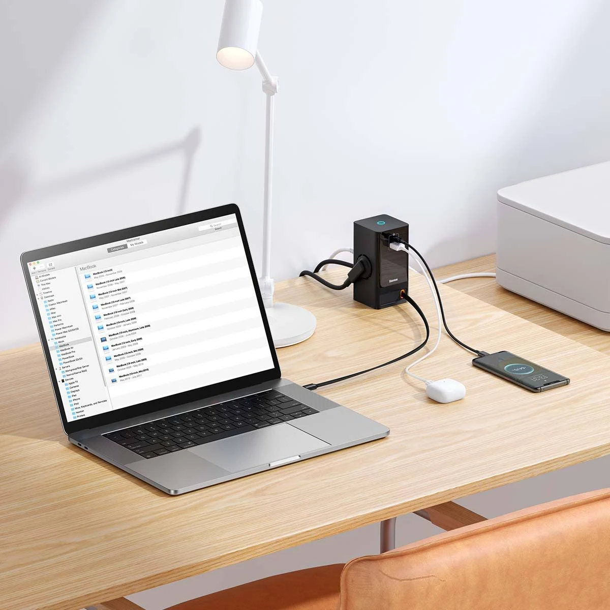 Laptop, regleta, smartphone y lámpara de escritorio sobre un escritorio de madera. Cables negros.