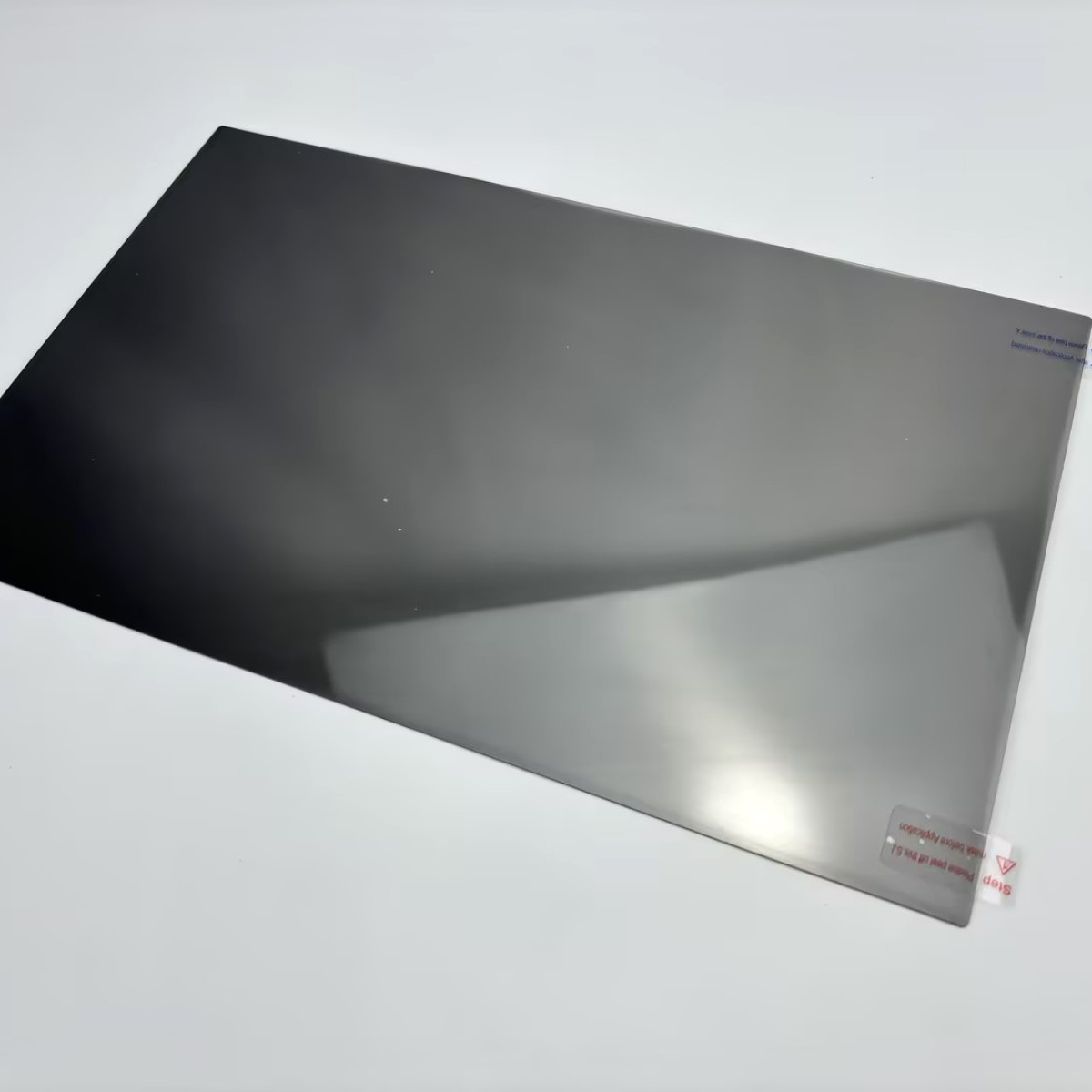 Uno schermo rettangolare grigio scuro con un adesivo staccabile. Sfondo bianco.