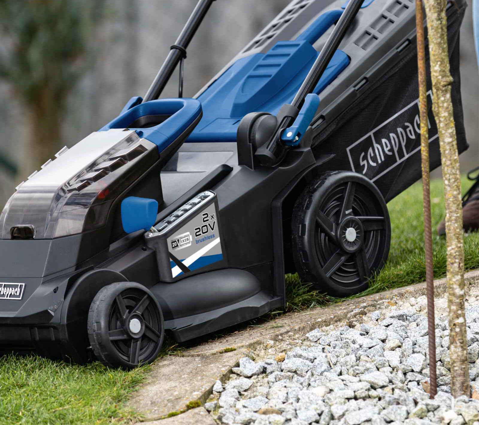 Een Scheppach grasmaaier, blauw en zwart, op groen gras. Een batterijpack is bevestigd.