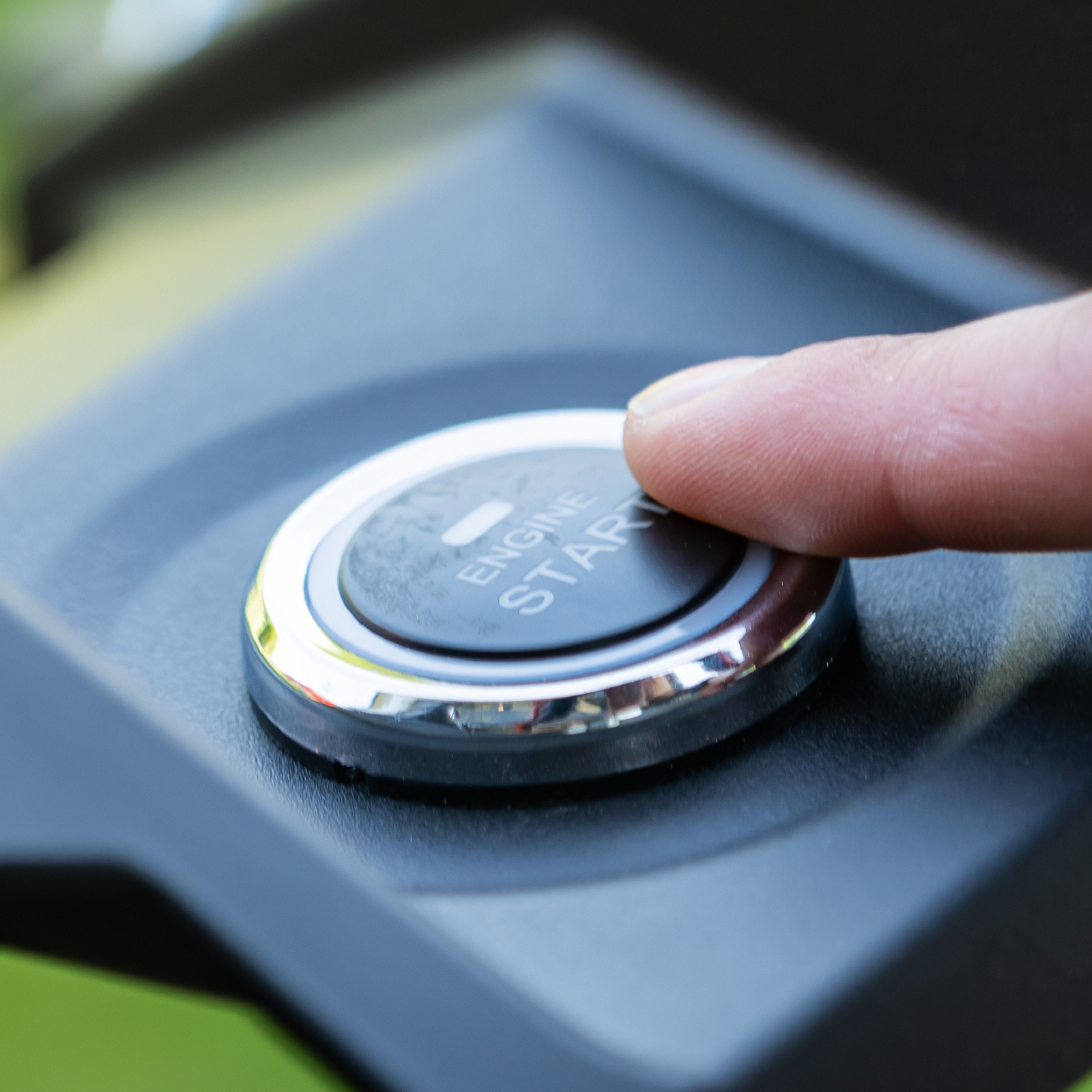 Vinger drukt op een zwarte knop met het woord 'ENGINE START'. Close-up.