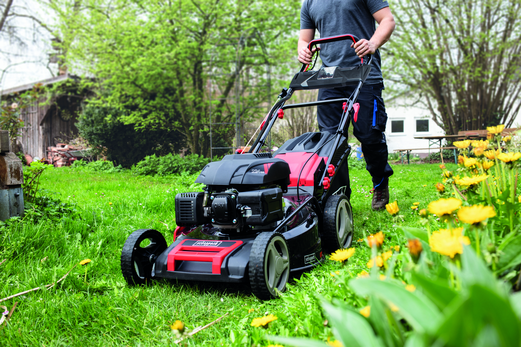 Een persoon die gras maait met een rood-zwarte grasmaaier in een tuin.