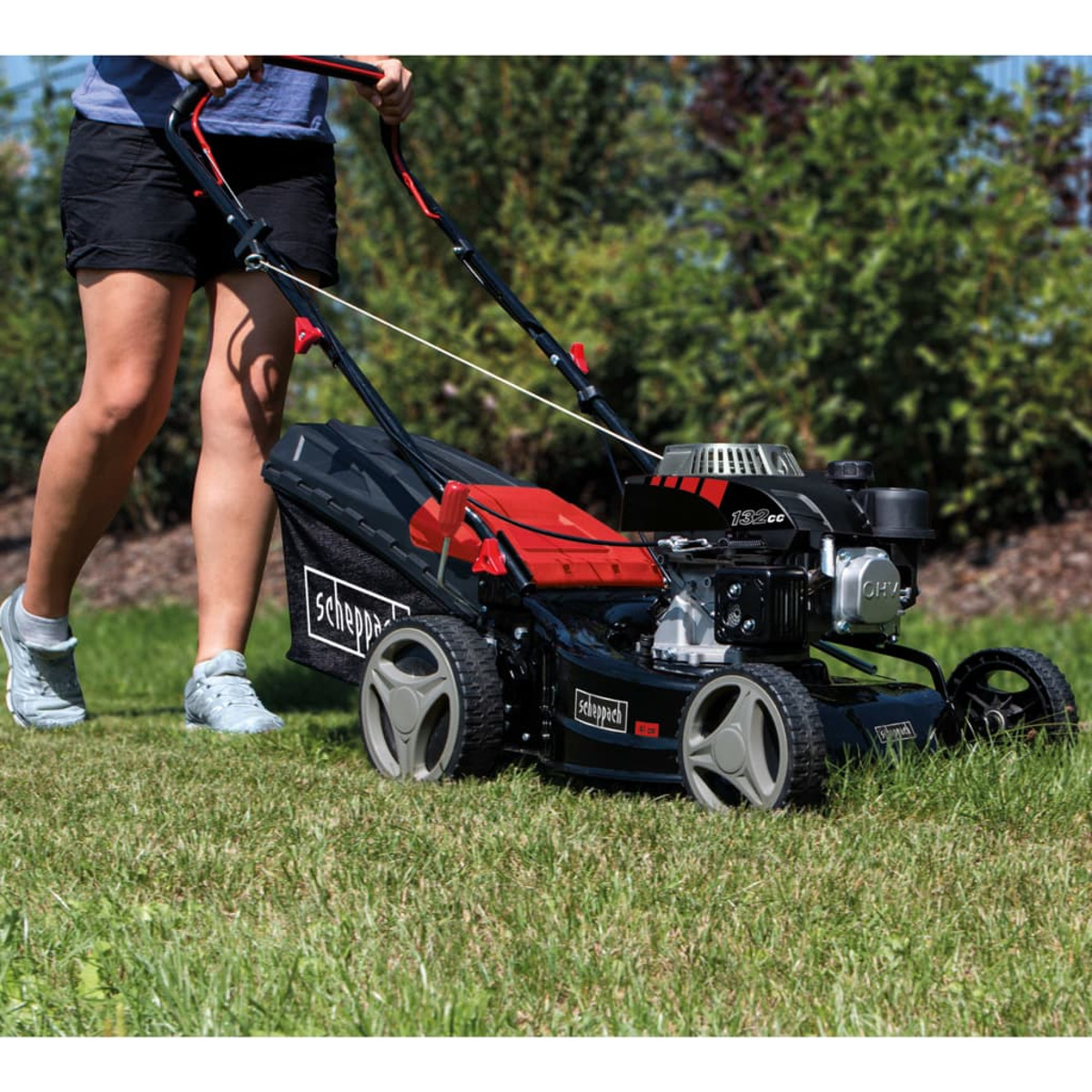 Een persoon maait het gras met een grasmaaier. De grasmaaier is rood.
