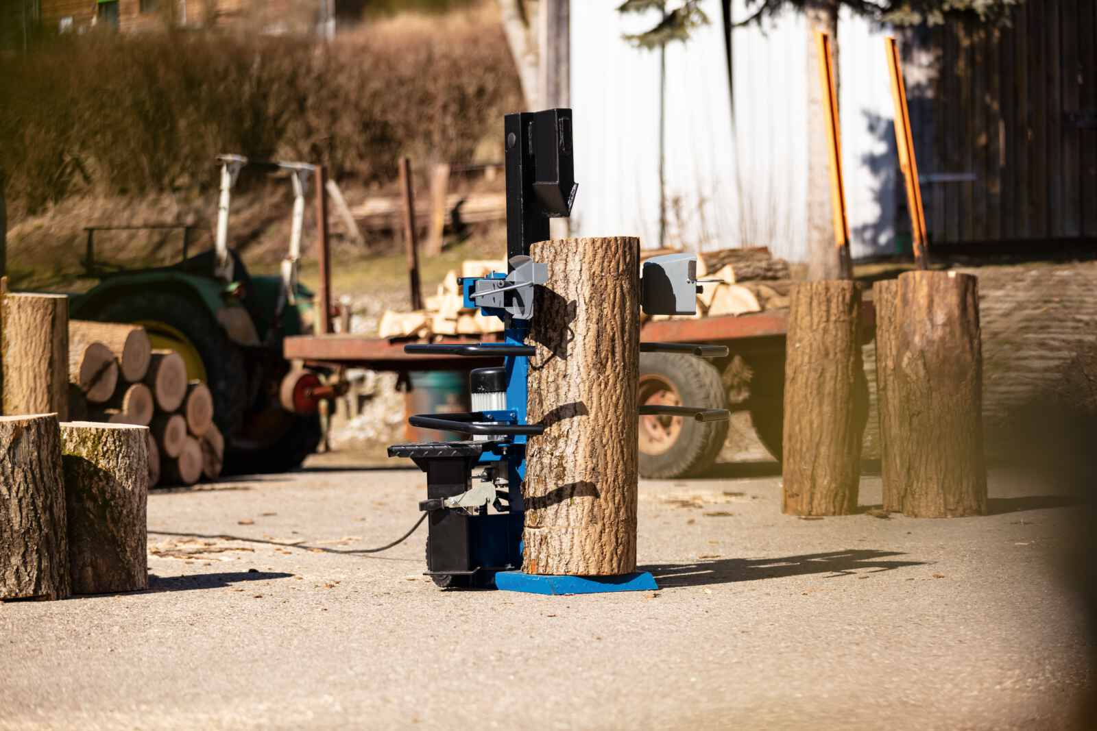 Een houtklover die een blok hout splijt. De machine is blauw en zwart, de blokken zijn bruin.