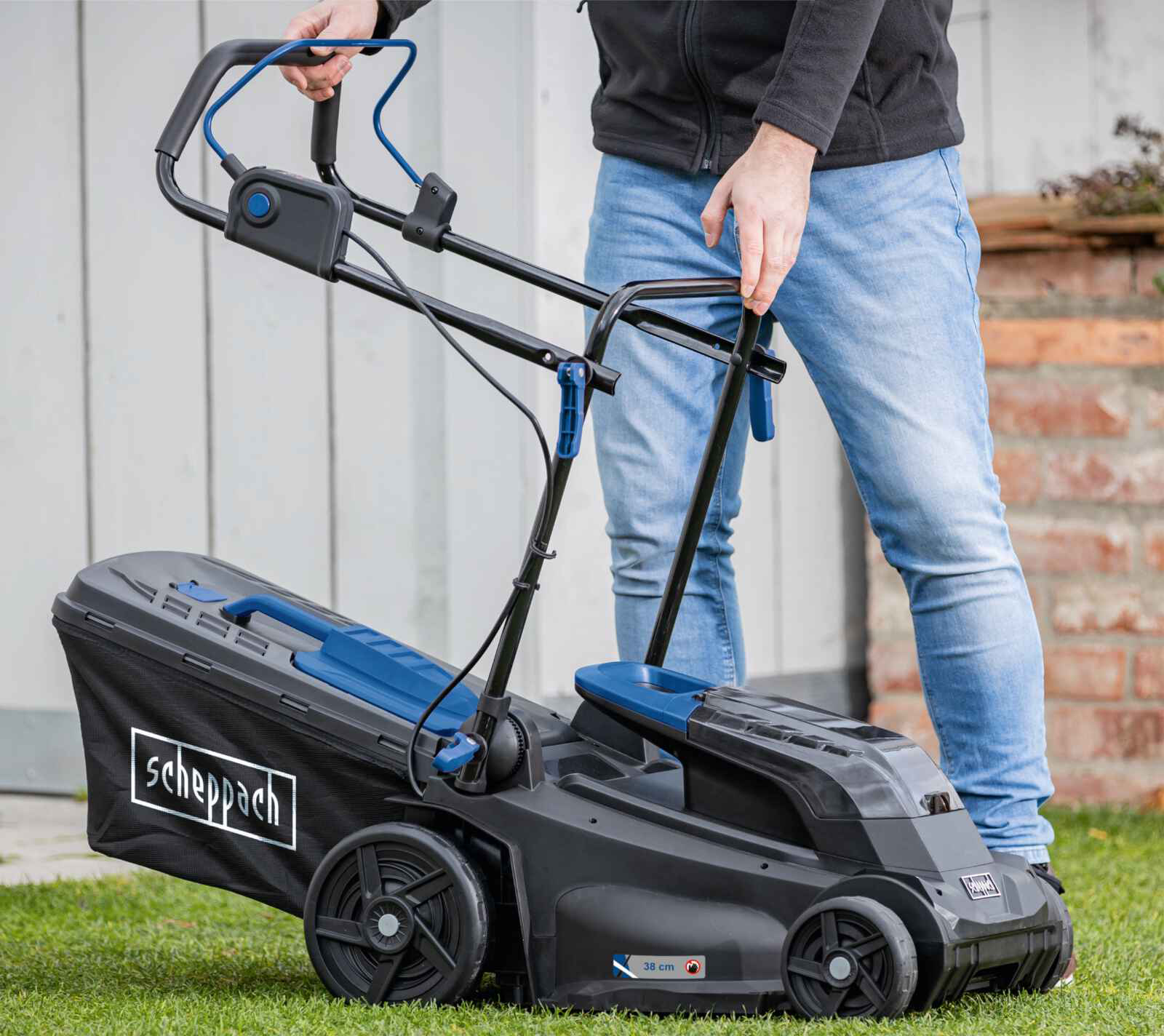 Eine Person mäht den Rasen mit einem schwarz-blauen Rasenmäher auf grünem Gras.