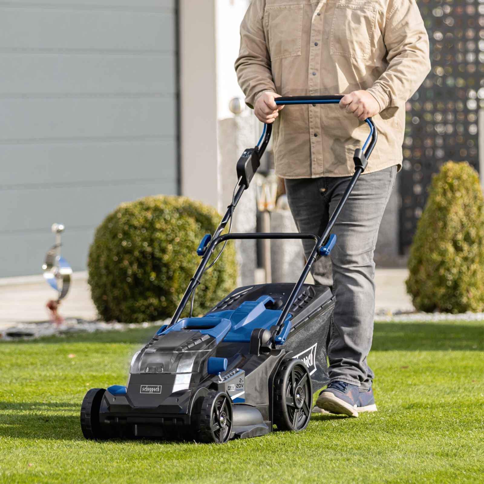 Man die gras maait met een zwart-blauwe elektrische grasmaaier. Groen gras en een huis op de achtergrond.