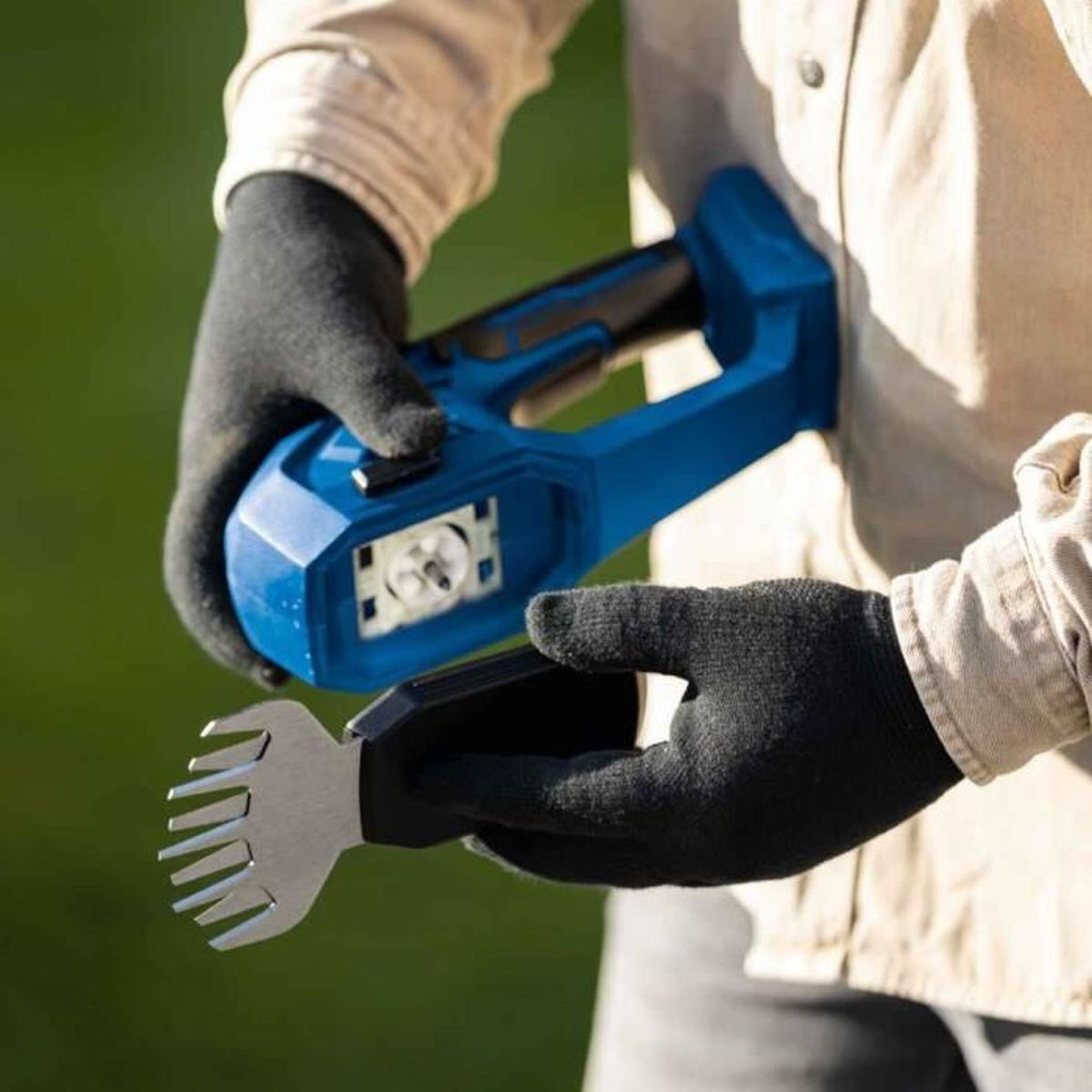 Persona che tiene in mano un attrezzo da giardino blu e nero. La persona indossa guanti neri.