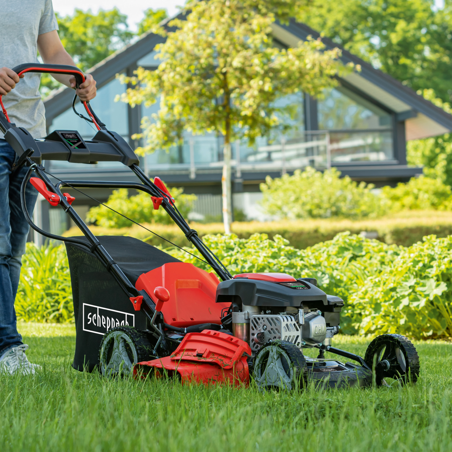 Man die gras maait met een rode en zwarte grasmaaier. Groen gras, een huis en bomen op de achtergrond.