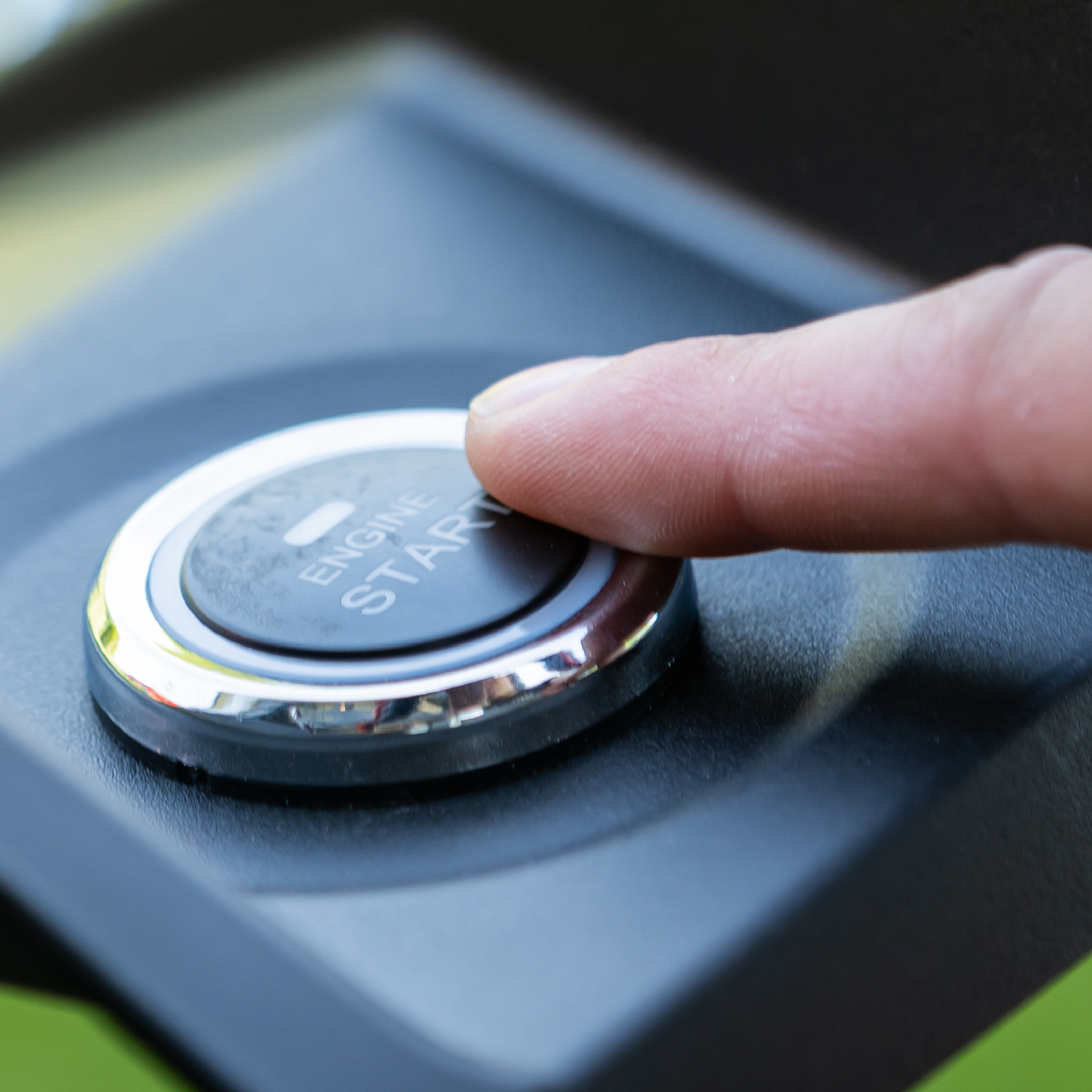 Vinger drukt op de startknop van de motor op een zwart oppervlak.