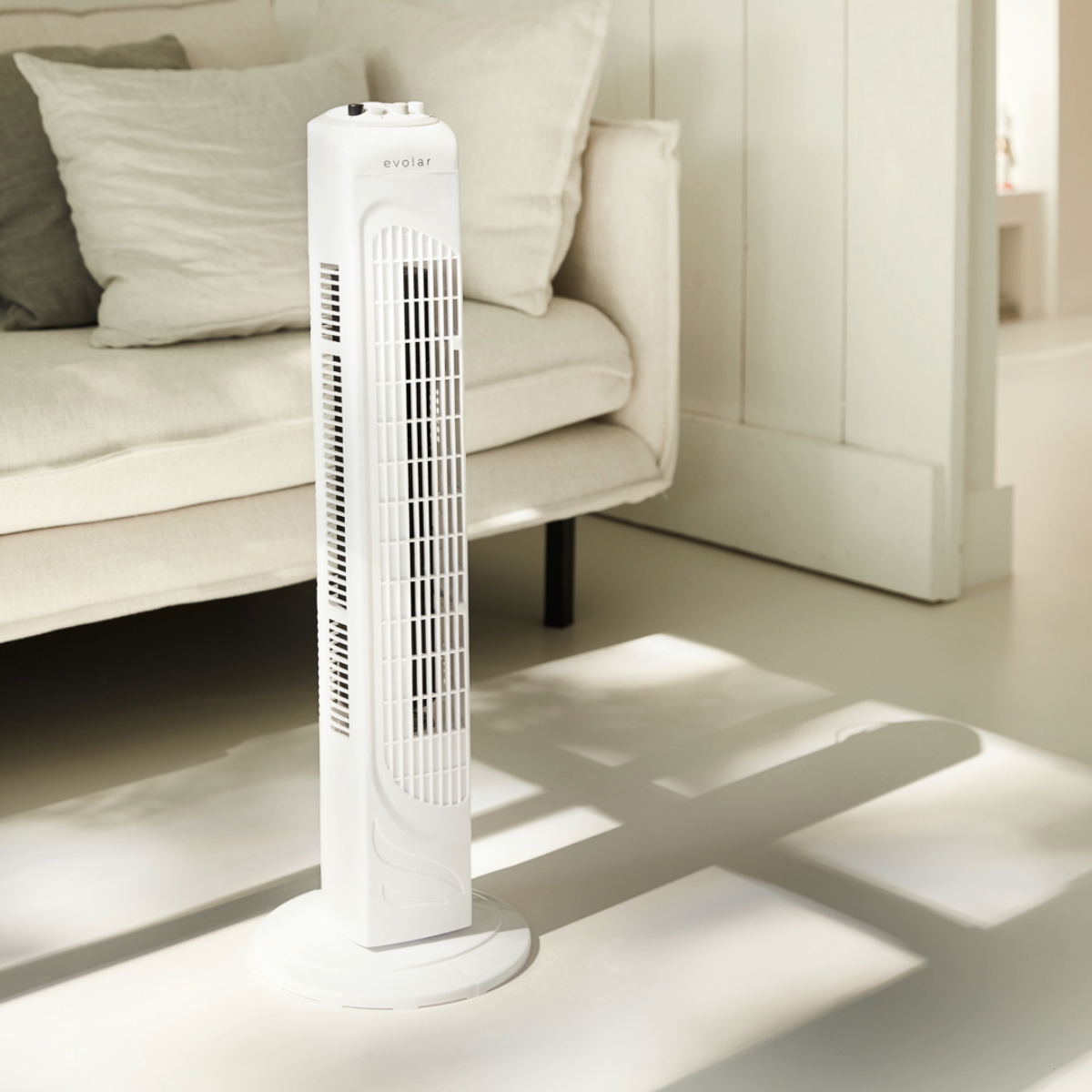White tower fan in a room with a couch.