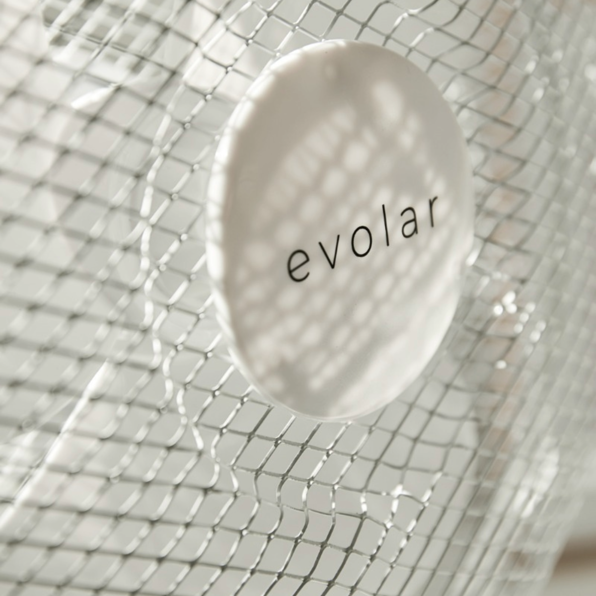 Een wit cirkelvormig label met 'evolar' in zwarte tekst, gezien door een zilveren gaas.