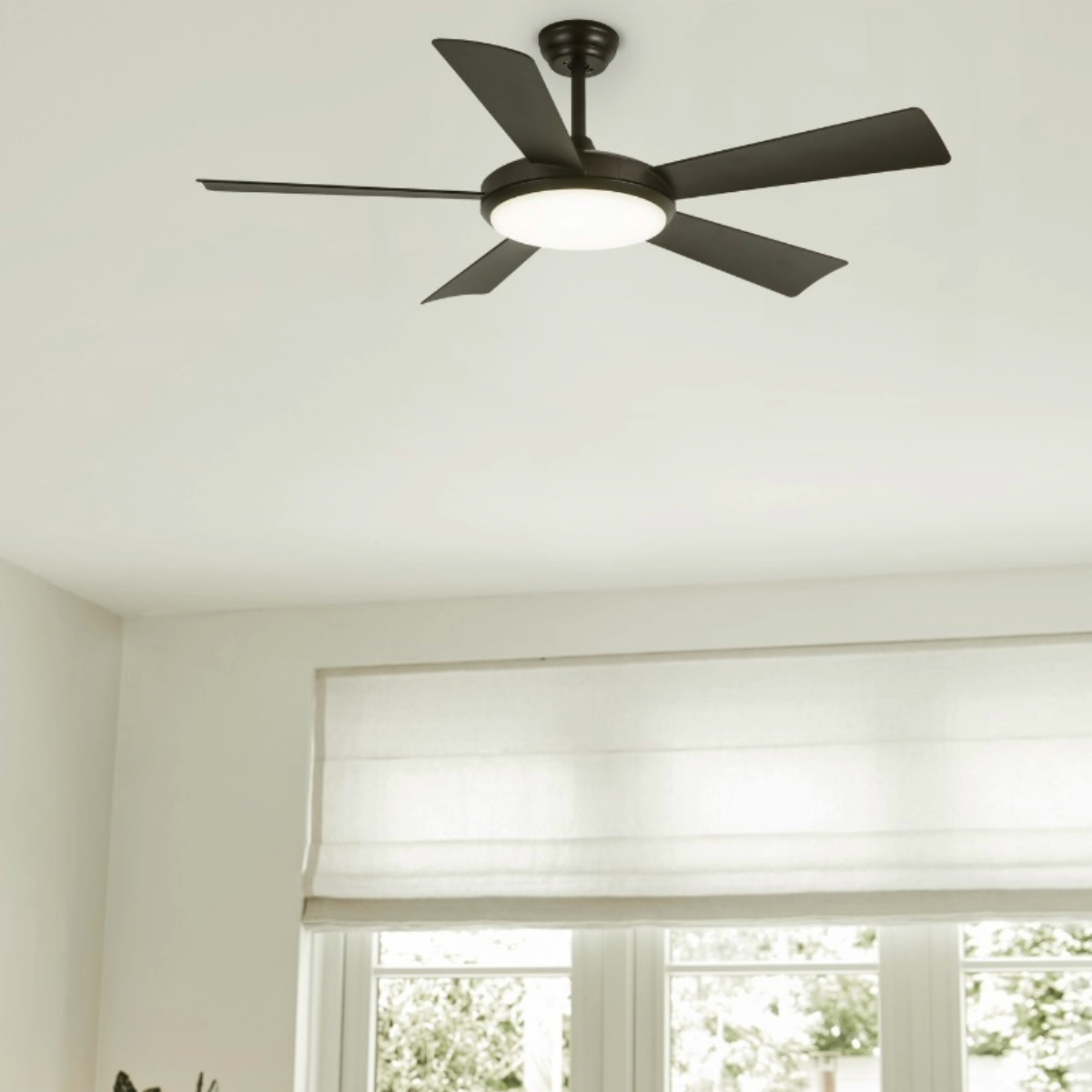 A dark brown ceiling fan with five blades and a central light fixture, in a room with a window.