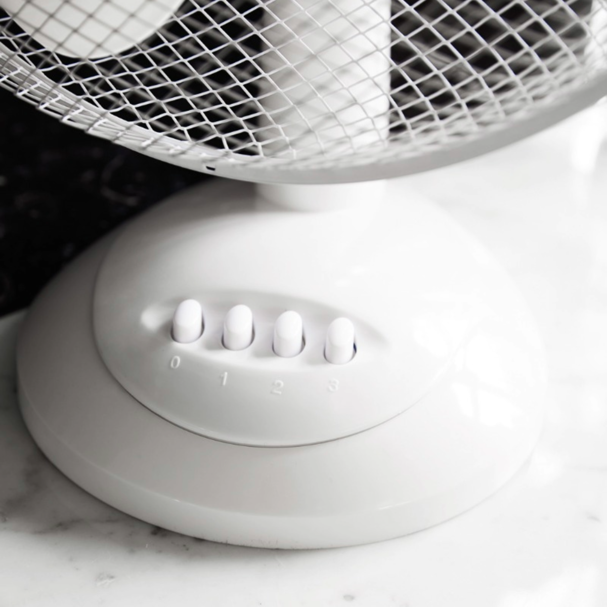 Close-up of a white desk fan with speed settings, numbered 0-3, on a marble surface.