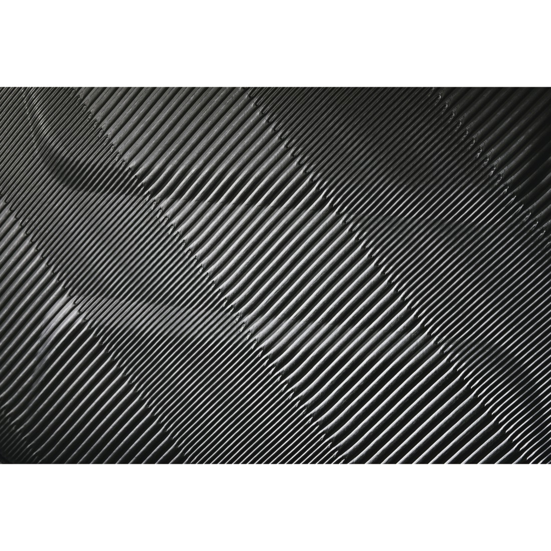 Schwarze, strukturierte Oberfläche mit diagonalen Linien. Die Linien erzeugen ein geripptes Muster.