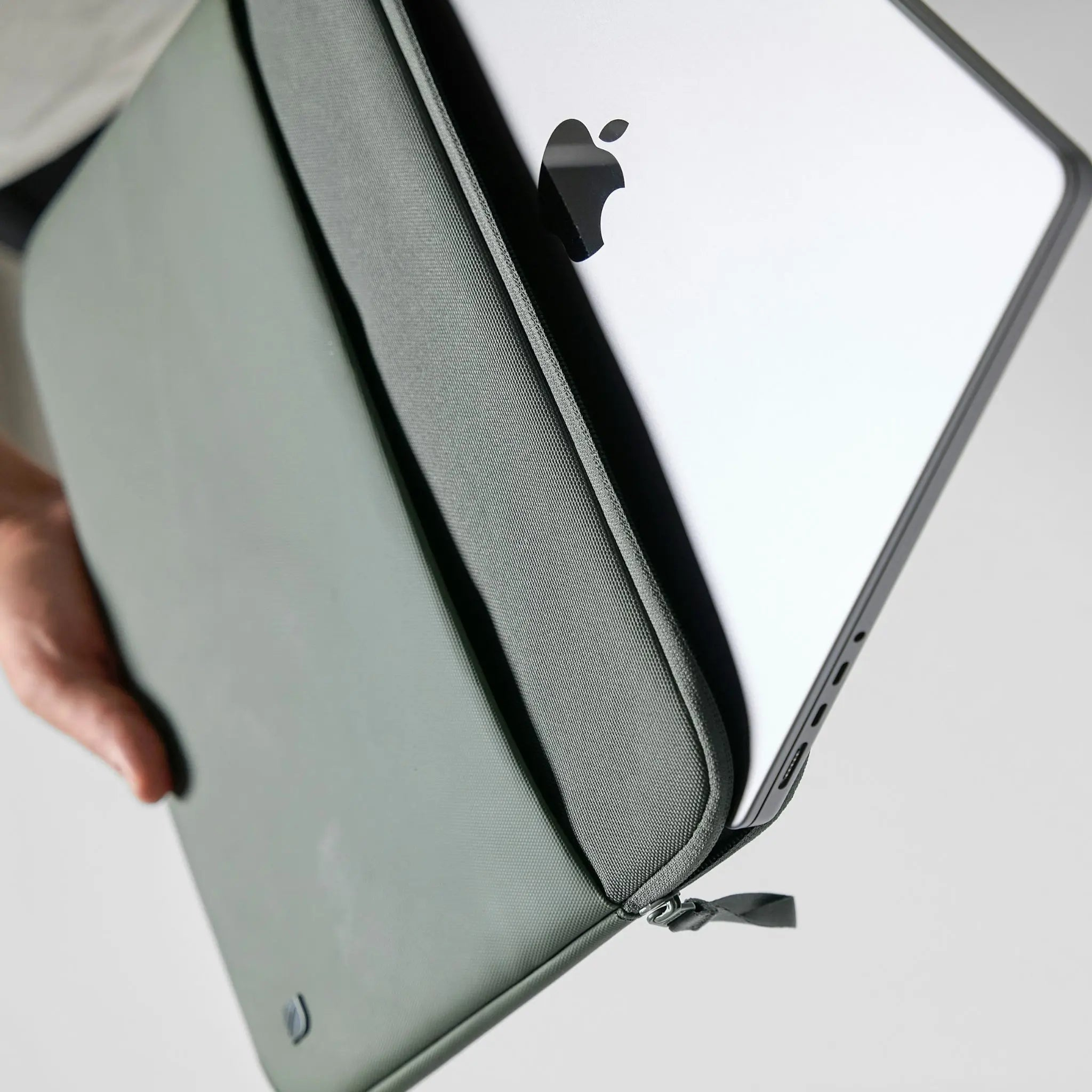 Custodia verde per laptop che tiene un laptop argentato con logo Apple, tenuto da una persona.
