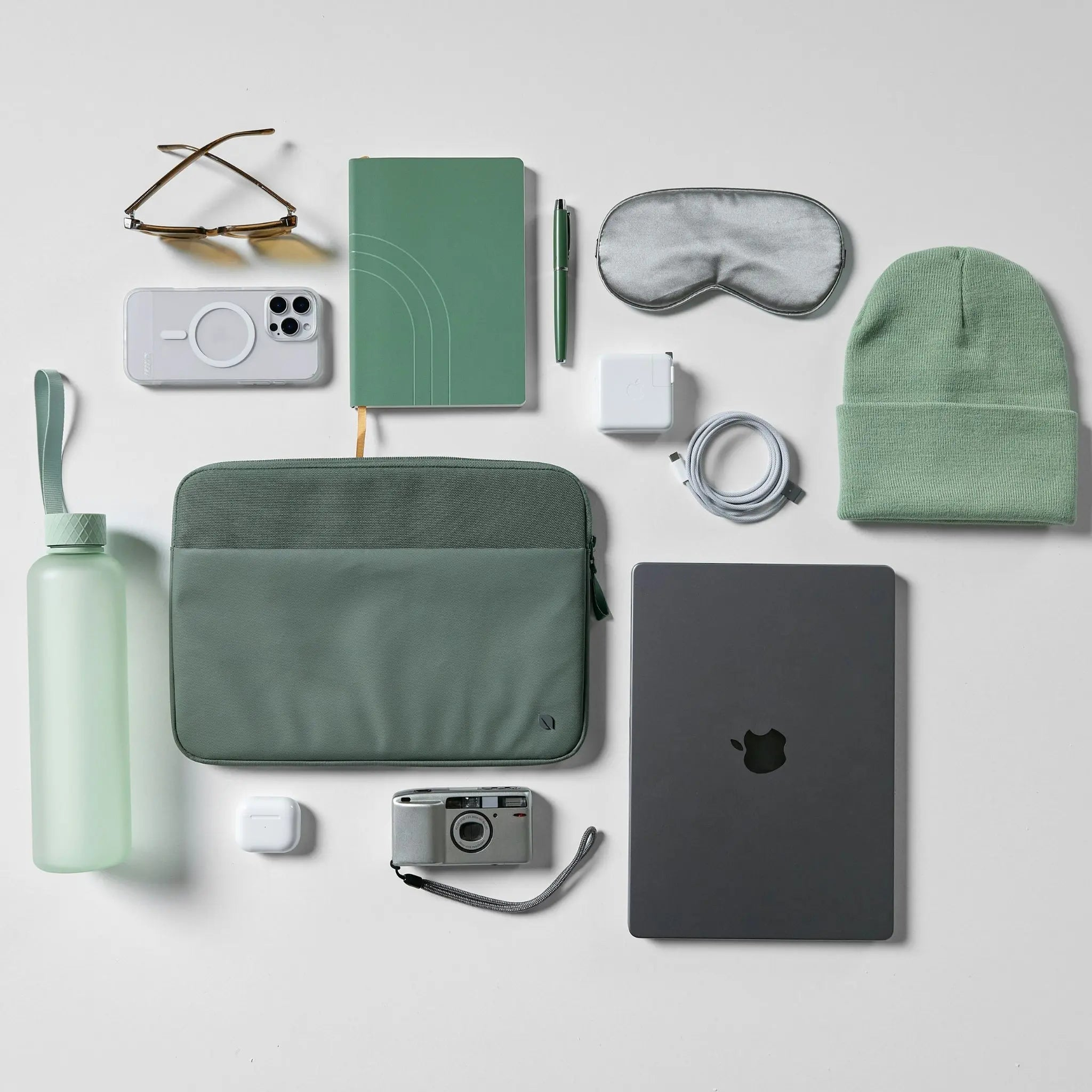 Una collezione di oggetti tecnologici e da viaggio: laptop, fotocamera, cuffie, occhiali, quaderno e bottiglia d'acqua.