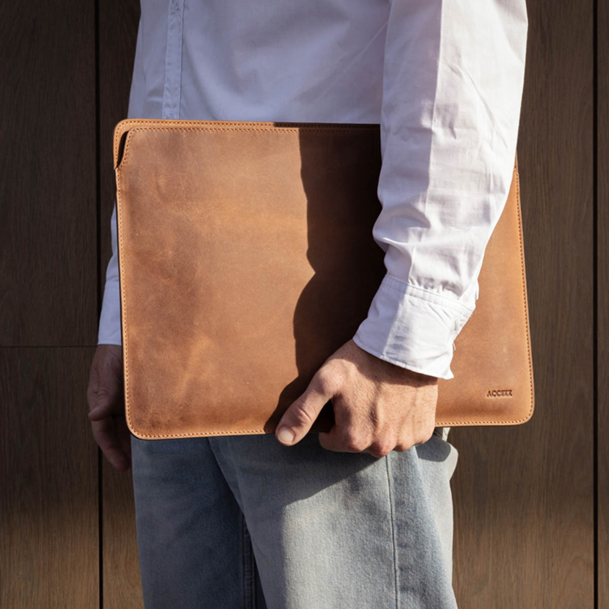 A person holding a brown leather laptop sleeve. The brand name ACCEE is visible.
