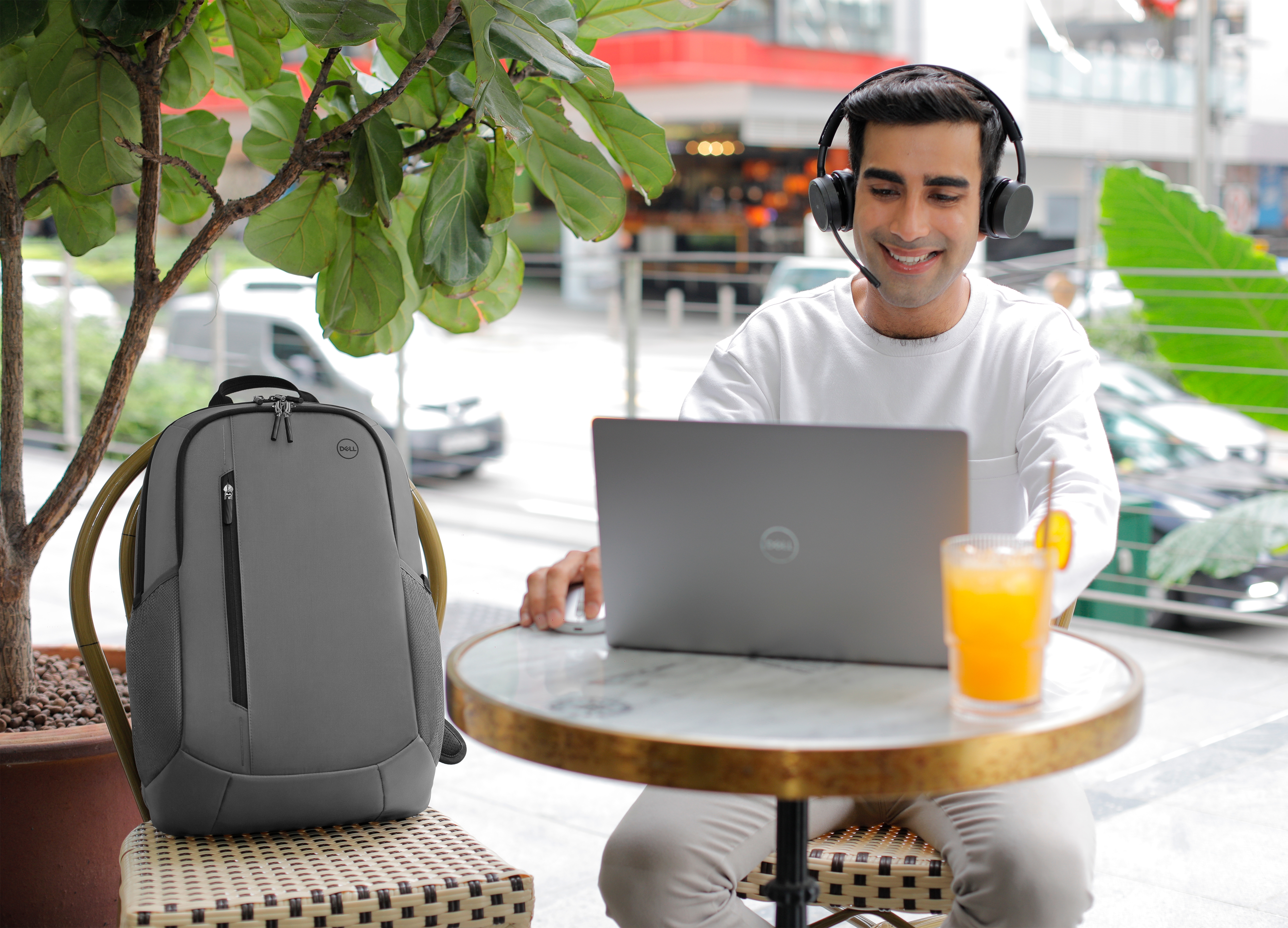 Uomo usa laptop all'aperto, con cuffie, zaino e succo su un tavolo.