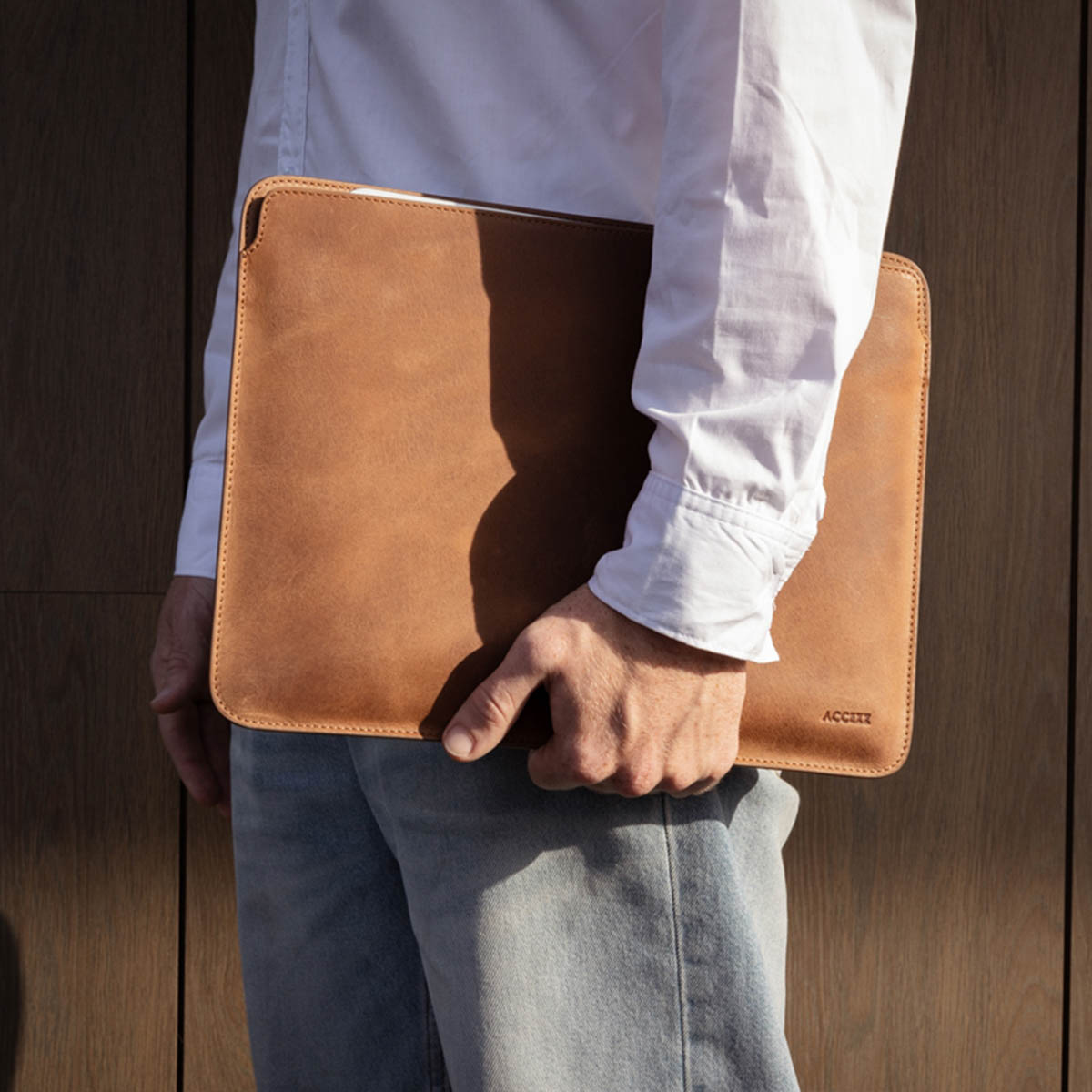 A person holding a brown leather laptop sleeve.
