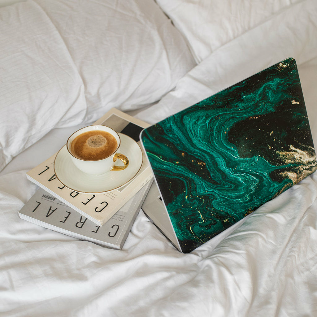 Laptop sul letto con caffè e libri. Il laptop ha un design a marmo verde.