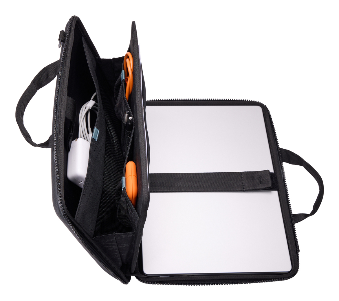 Borsa per laptop nera aperta, con laptop, caricatore e altri oggetti visibili. Sfondo bianco.