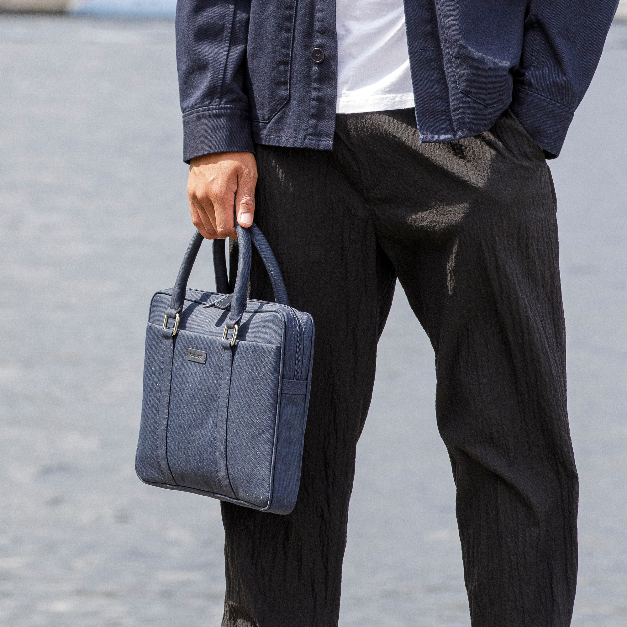Uomo che tiene una borsa blu per laptop. Indossa una giacca blu navy e pantaloni neri.