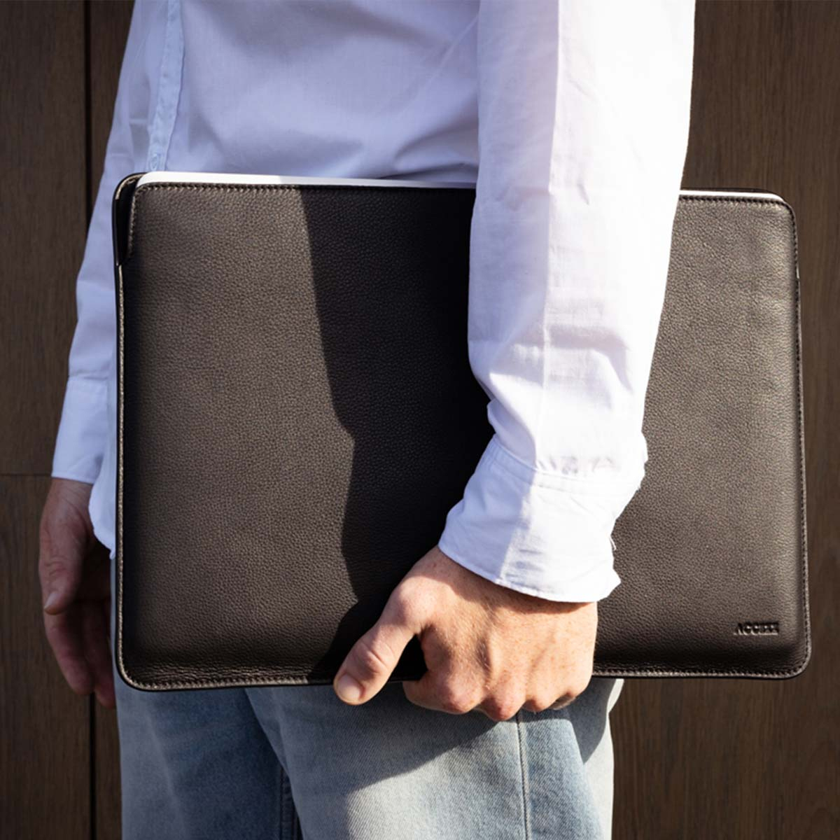 Person holding a dark brown leather laptop case, with a light-colored border.