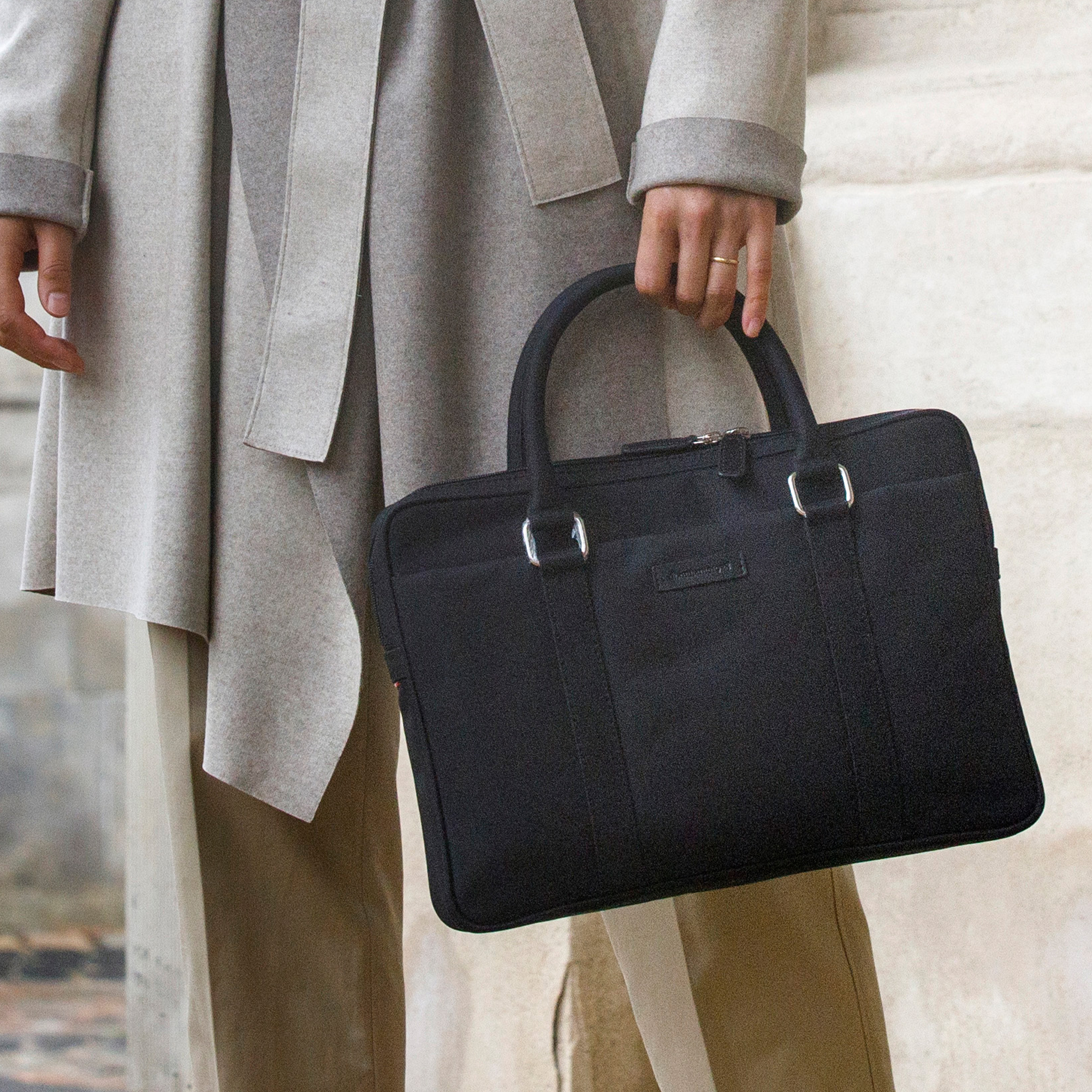 Persona che tiene una valigetta nera. La persona indossa un cappotto grigio e pantaloni kaki.