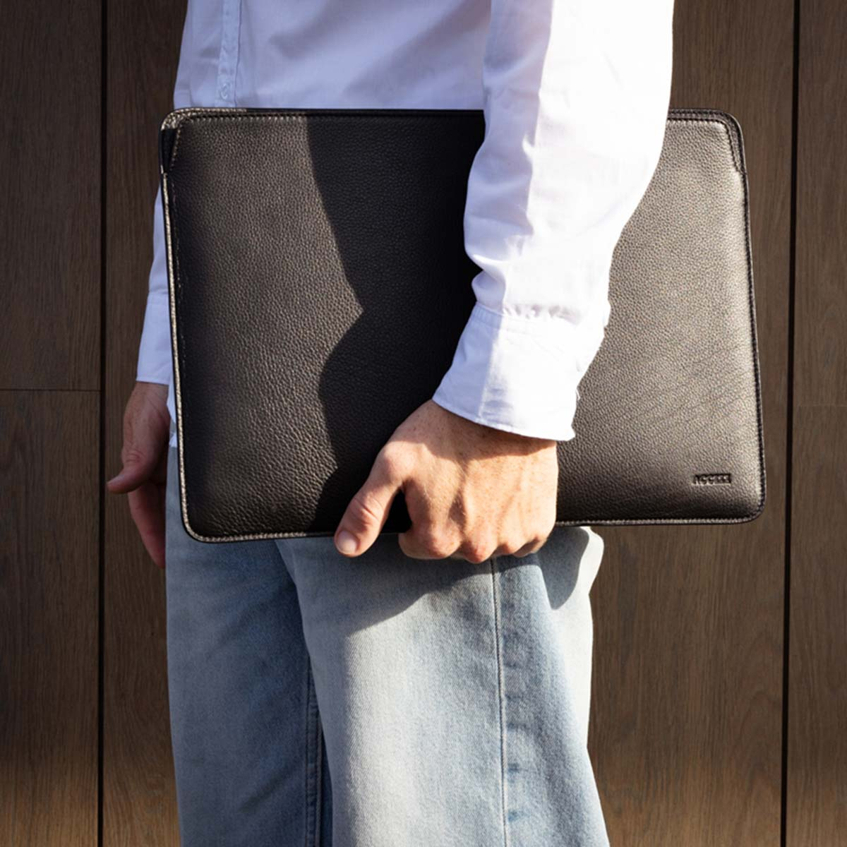A person holding a black leather laptop case. The case has a textured surface and is held close to the body.