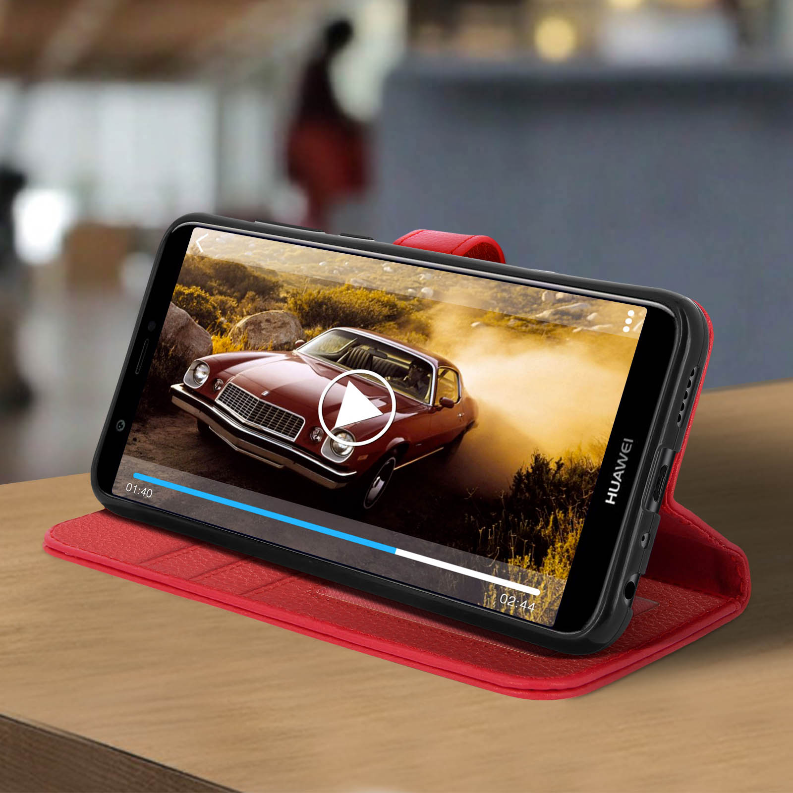 Uno smartphone con custodia rossa mostra un video. È su una superficie di legno. Lo sfondo è sfocato.